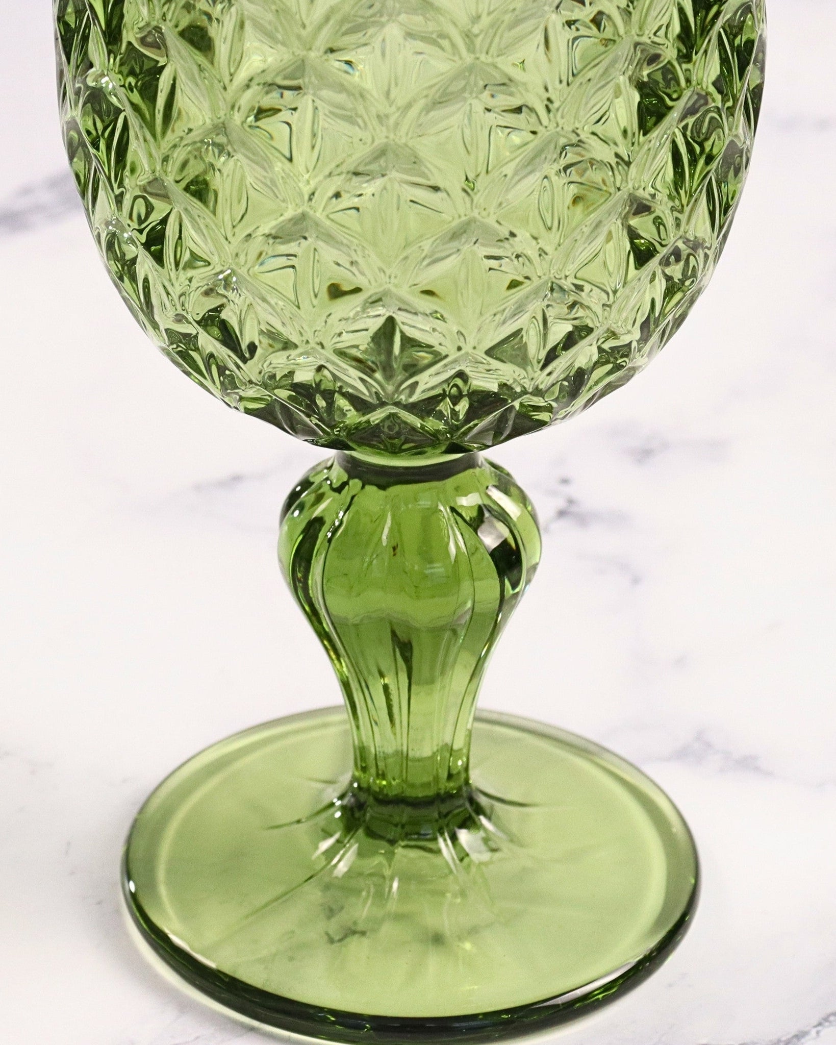Green glass goblet with textured design on a marble surface