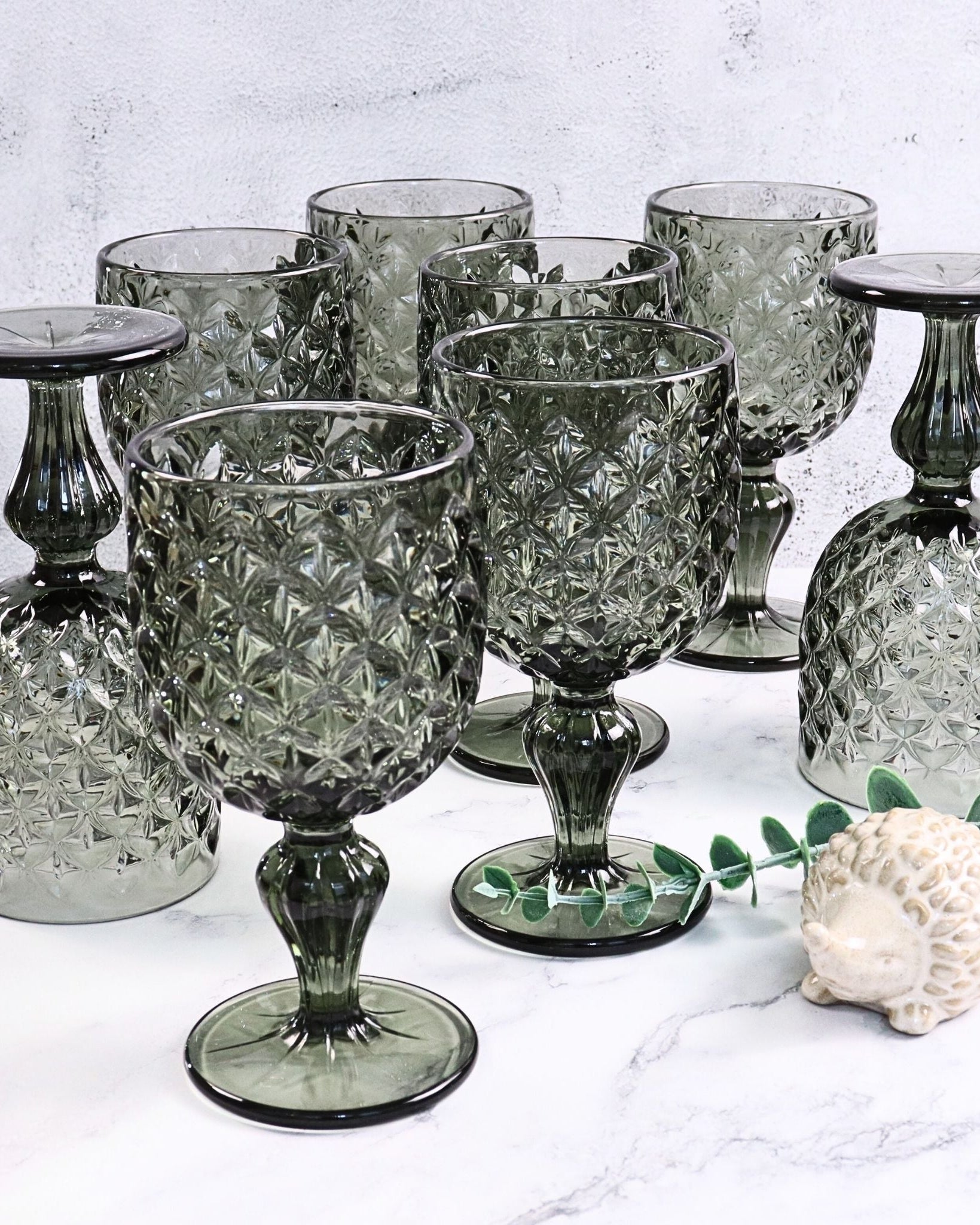 Set of grey glass goblets and candle holders on a white surface with a light grey background.