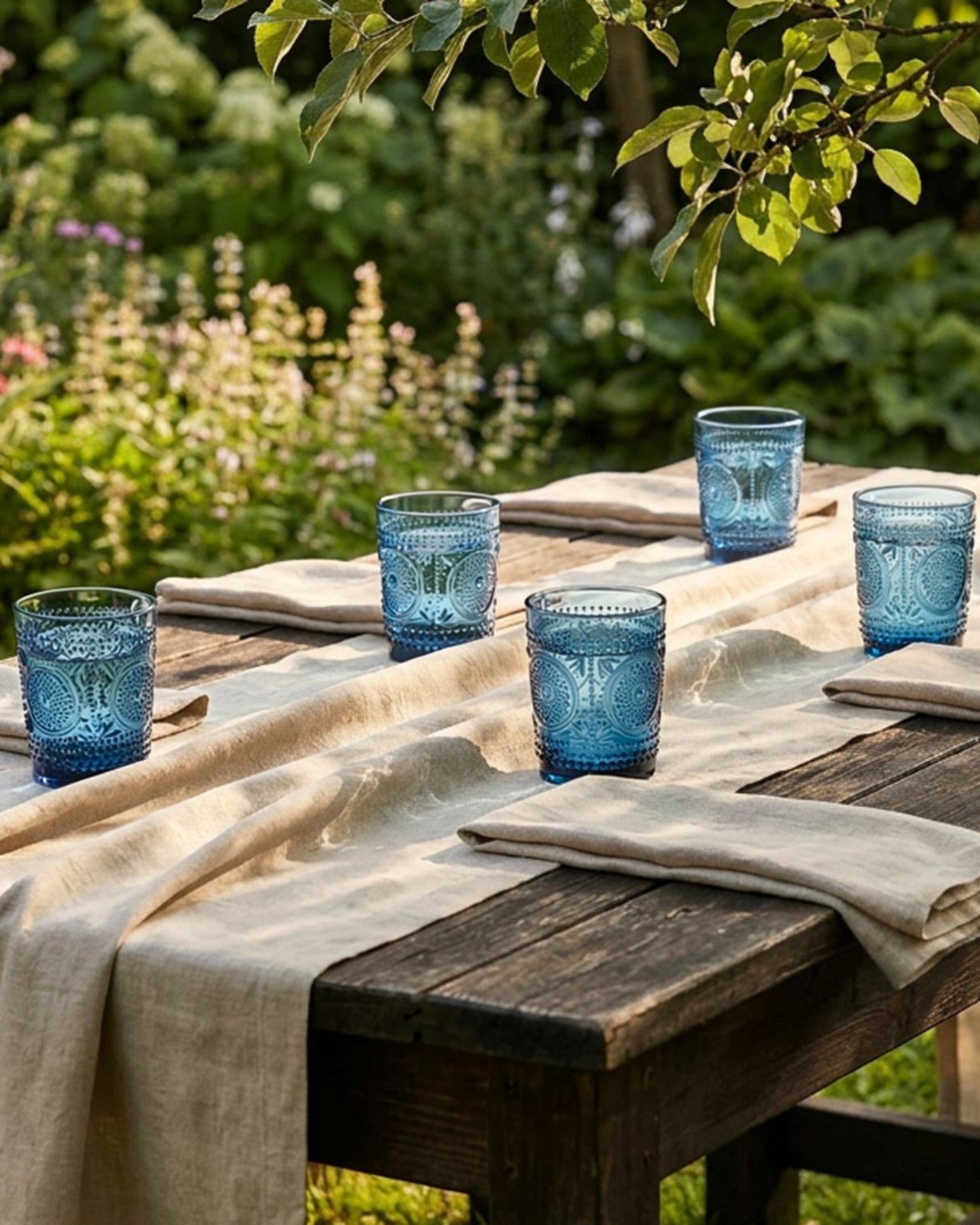 Two blue textured glass tumblers stacked on a white surface with a white curtain background.