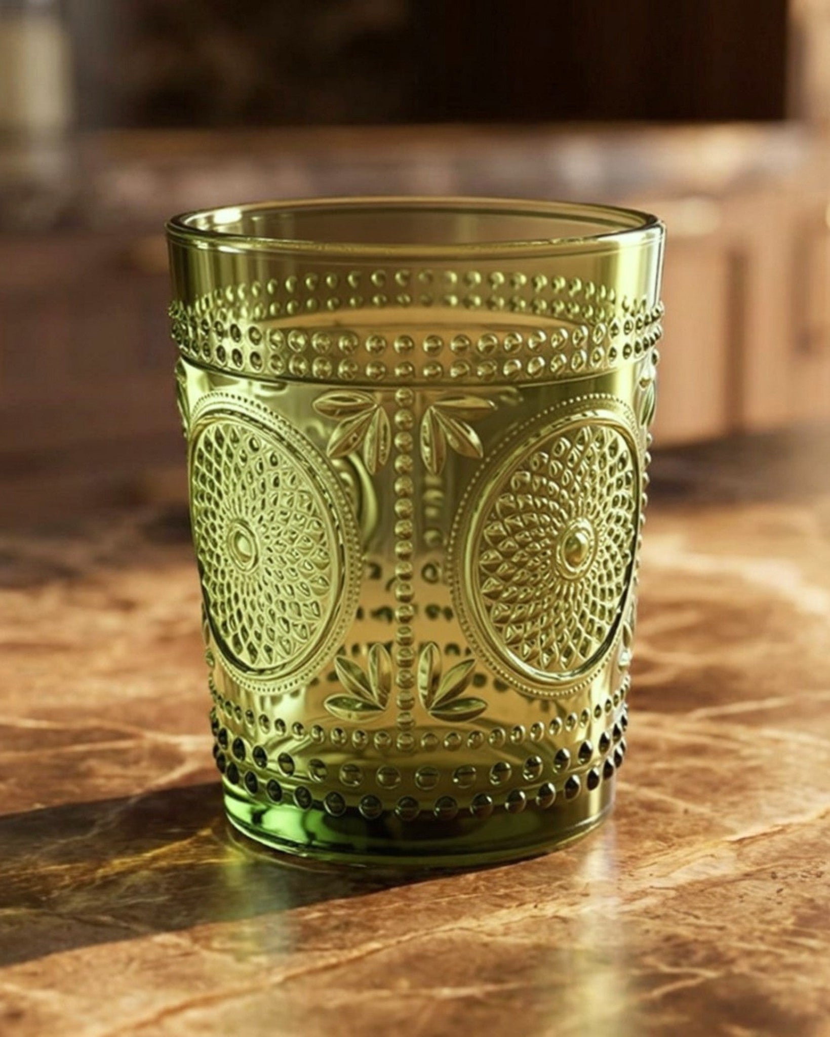 Set of green glass tumblers with embossed designs on a white surface.