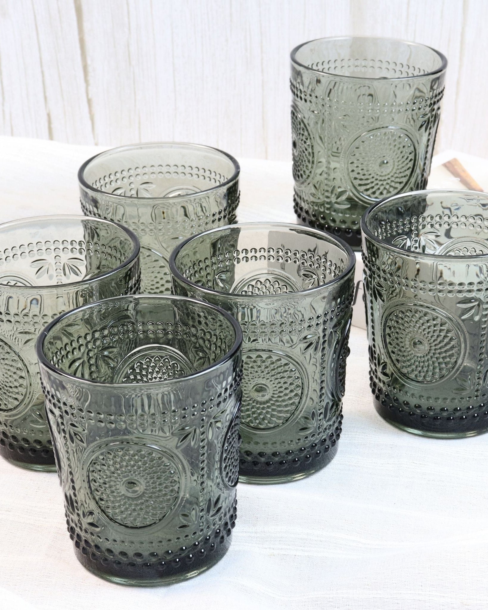 Set of six gray glass tumblers with embossed designs on a white surface.