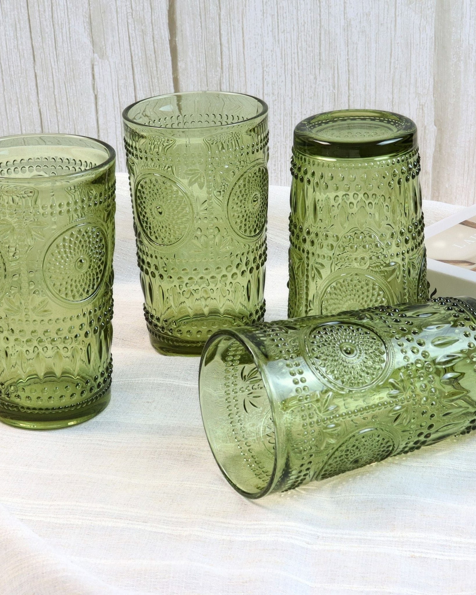 Set of four green patterned glass tumblers on a light surface with a white textured background.