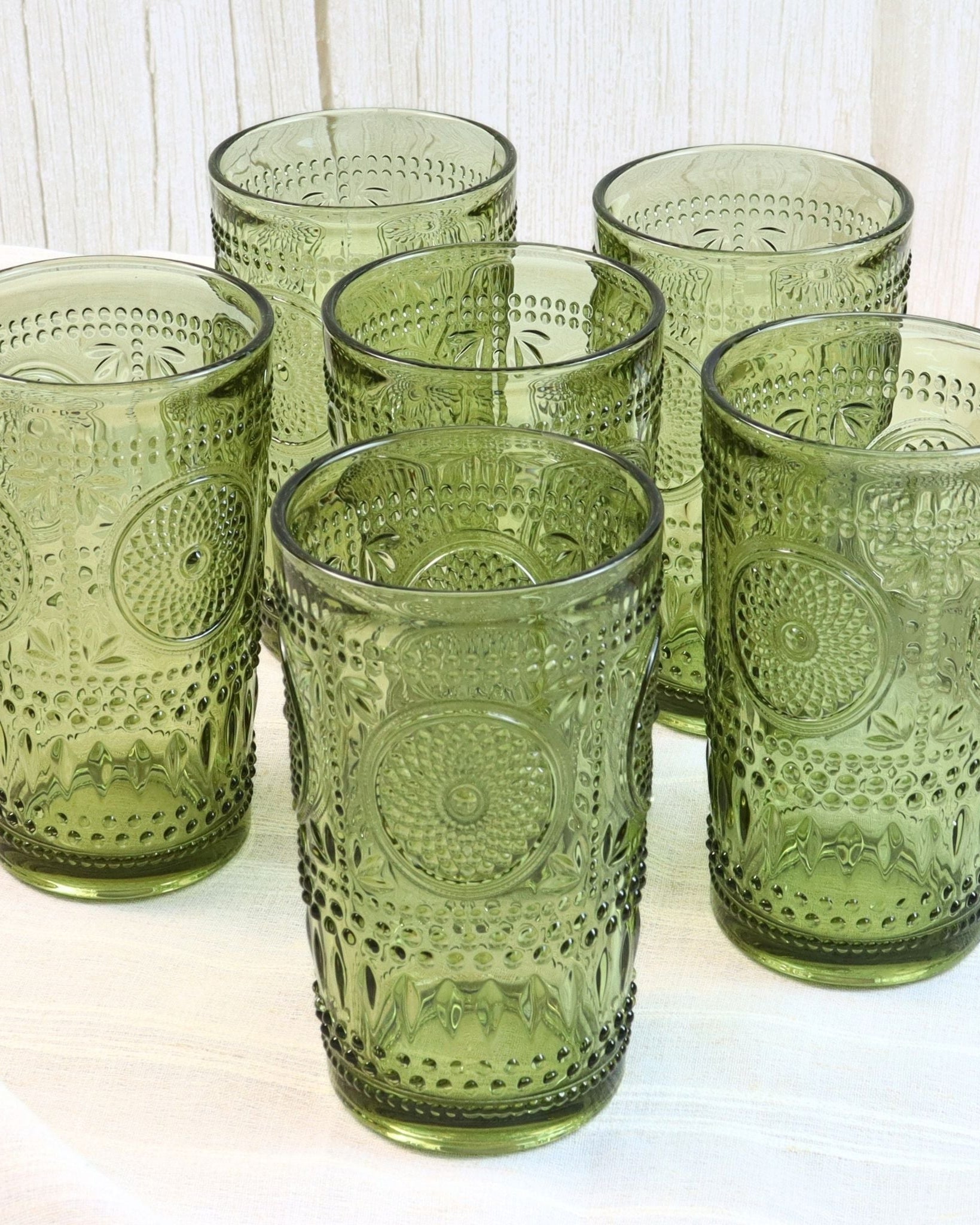 Set of six green glass tumblers with embossed designs on a white surface.