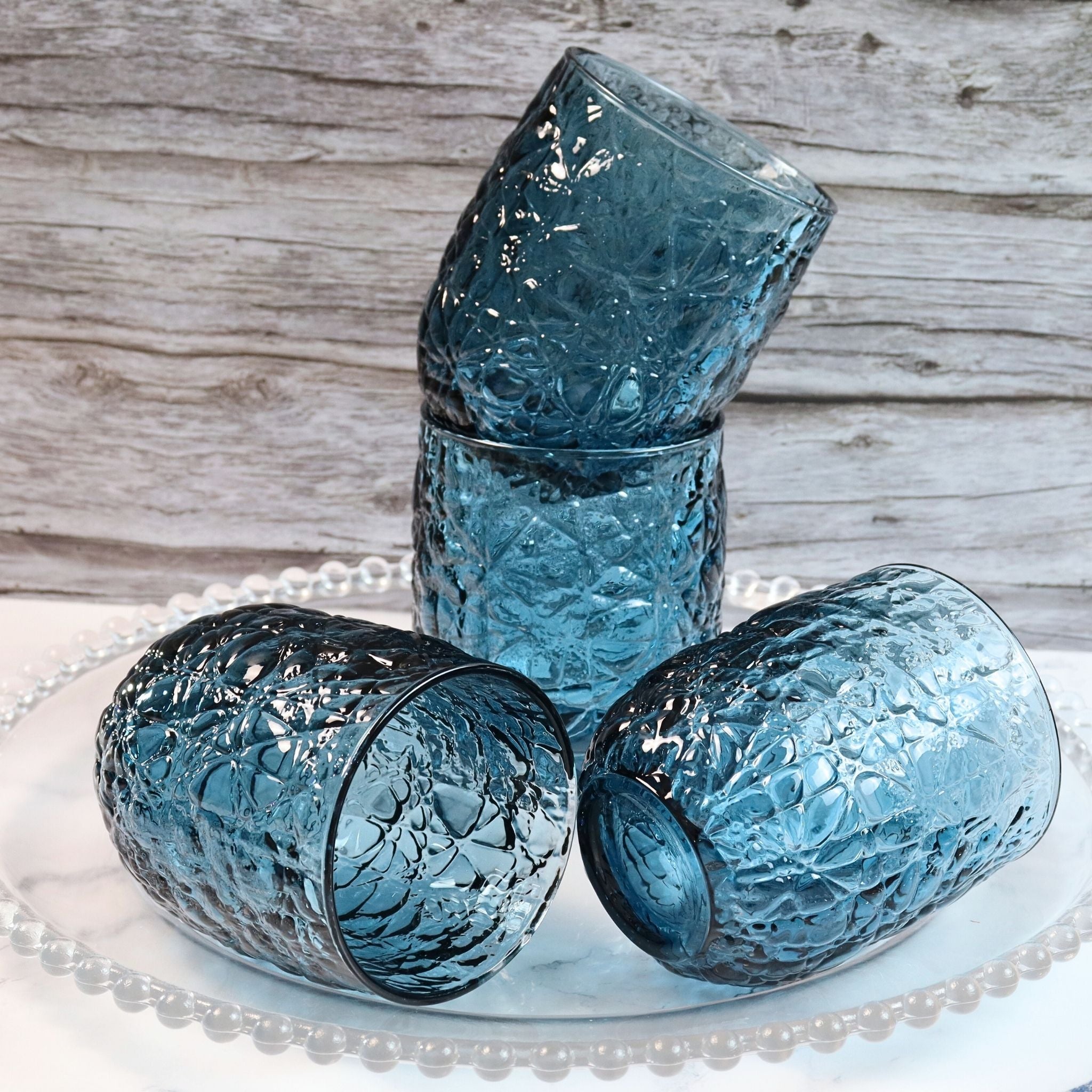 Set of four blue textured glass tumblers on a white lace doily with a wooden background.