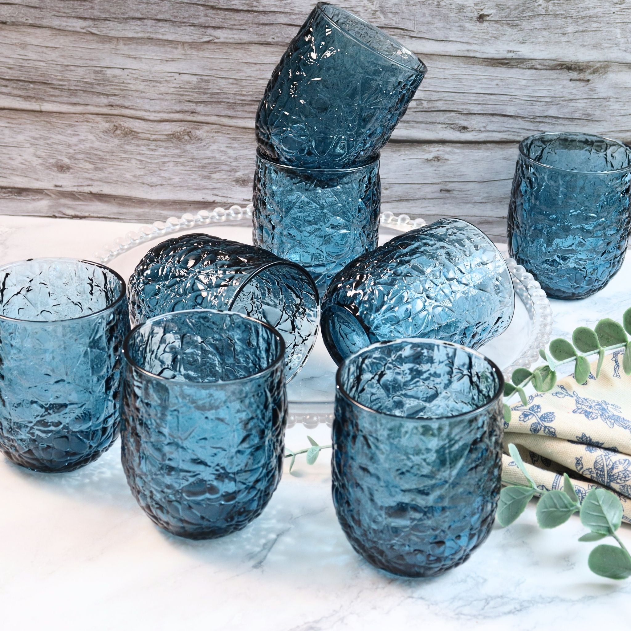 Set of blue textured glass tumblers on a white surface with a wooden background