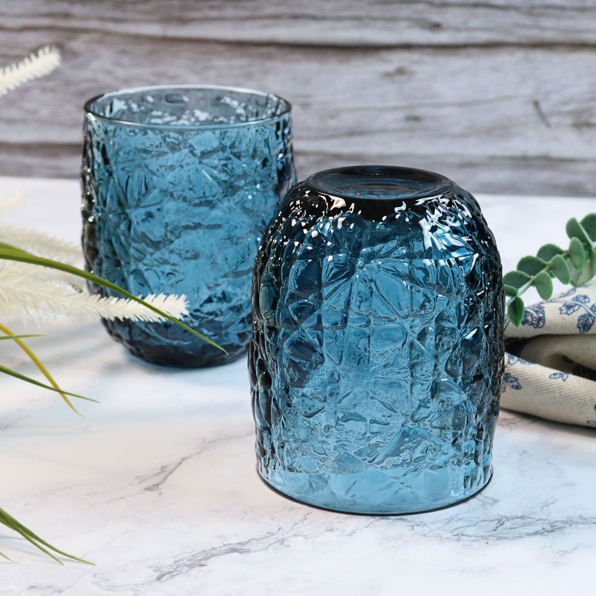 Two textured blue glass vases on a marble surface with a wooden background.