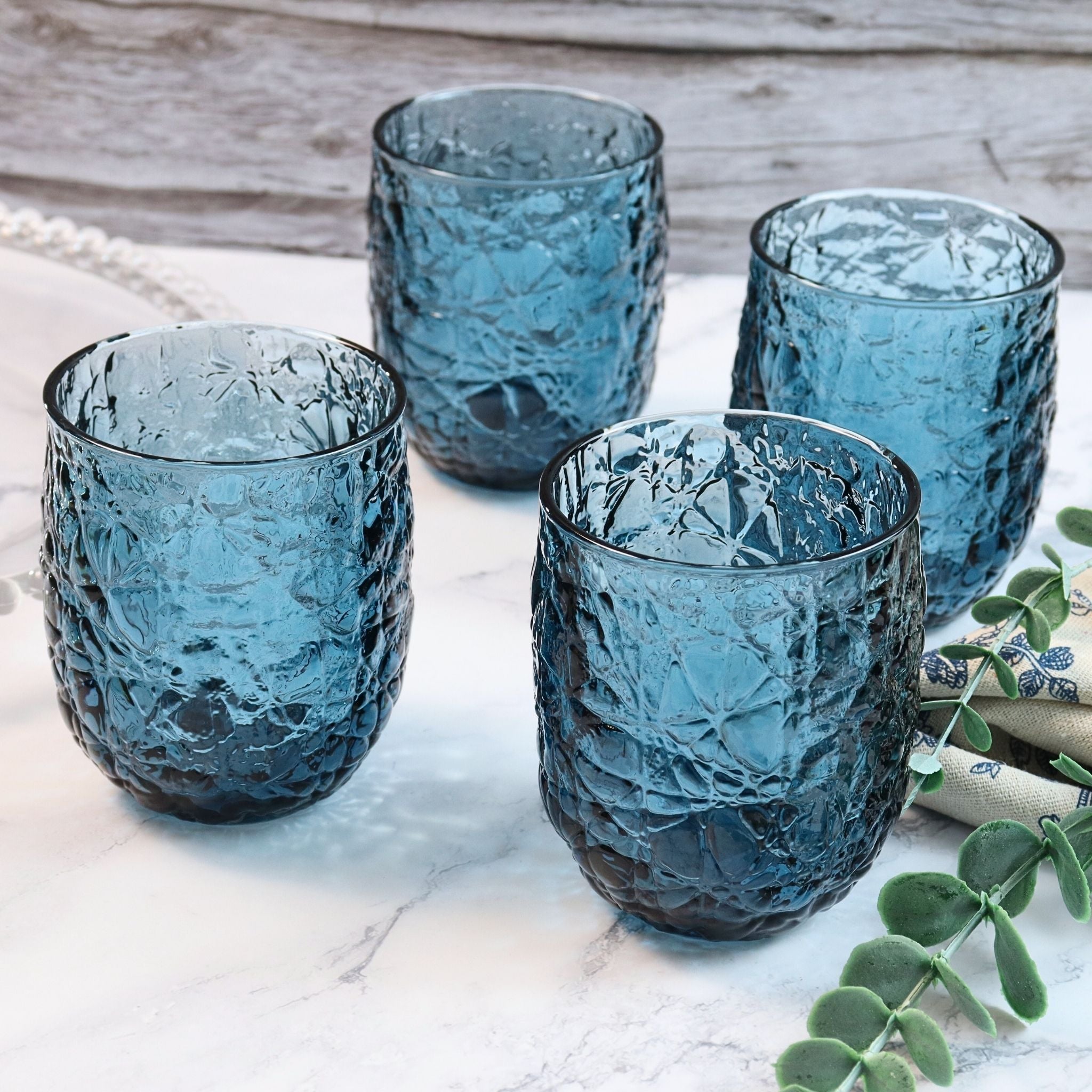 Set of four textured blue glasses on a marble surface with a wooden background