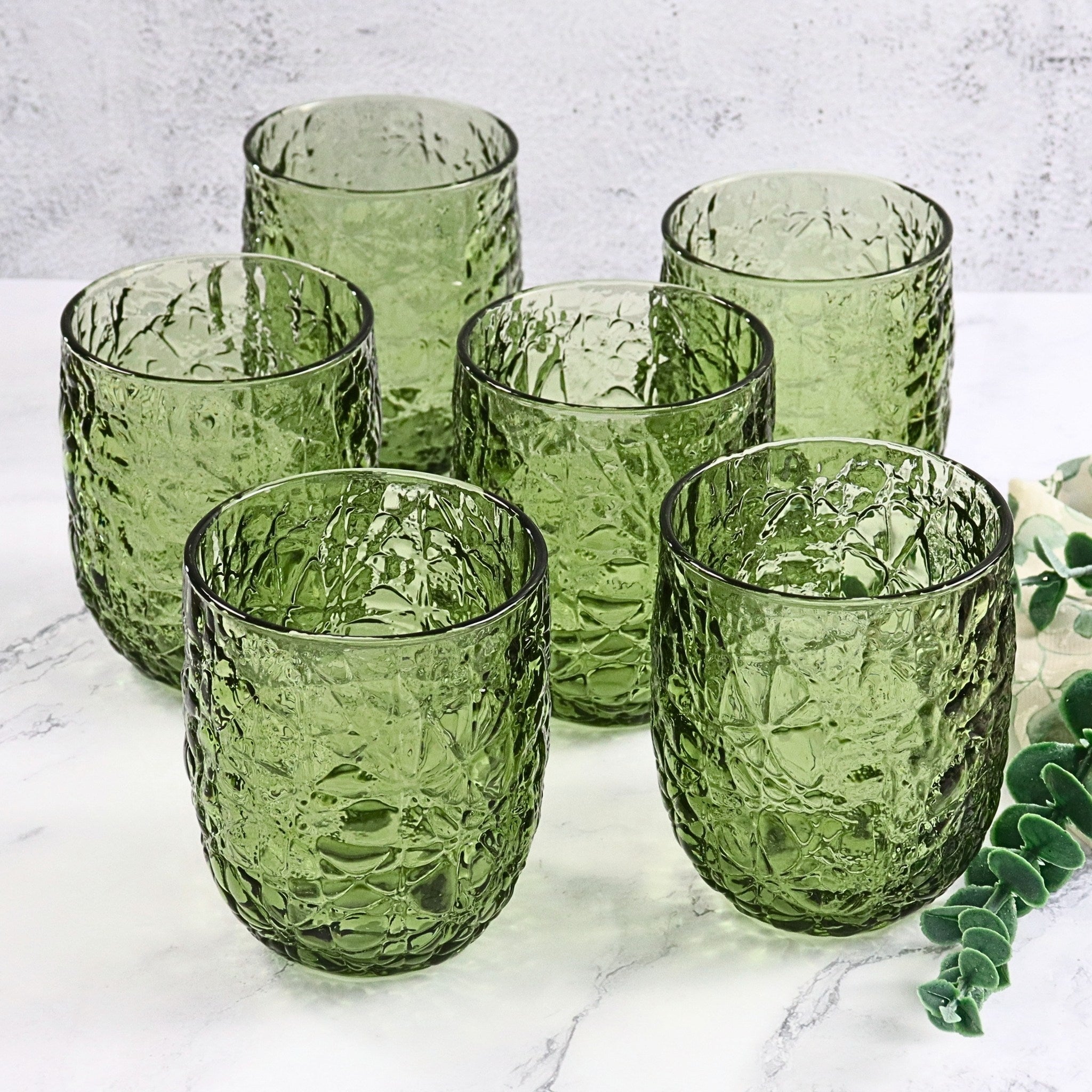 Set of six green textured glass tumblers on a marble surface.