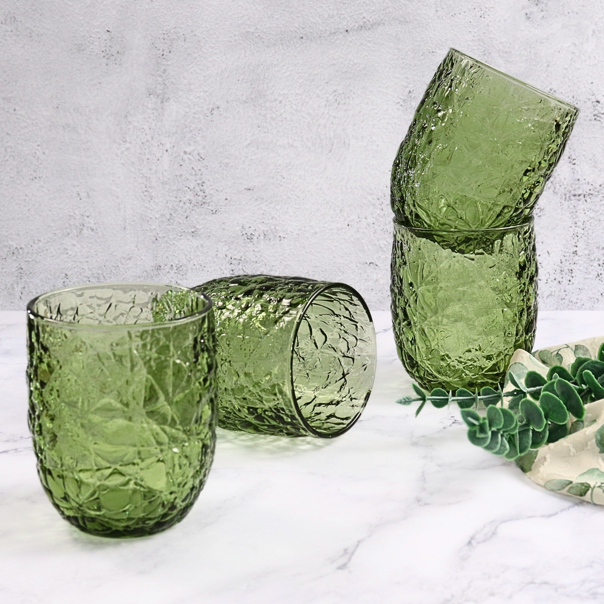 Green textured glass tumblers on a light gray surface with a plant in the background