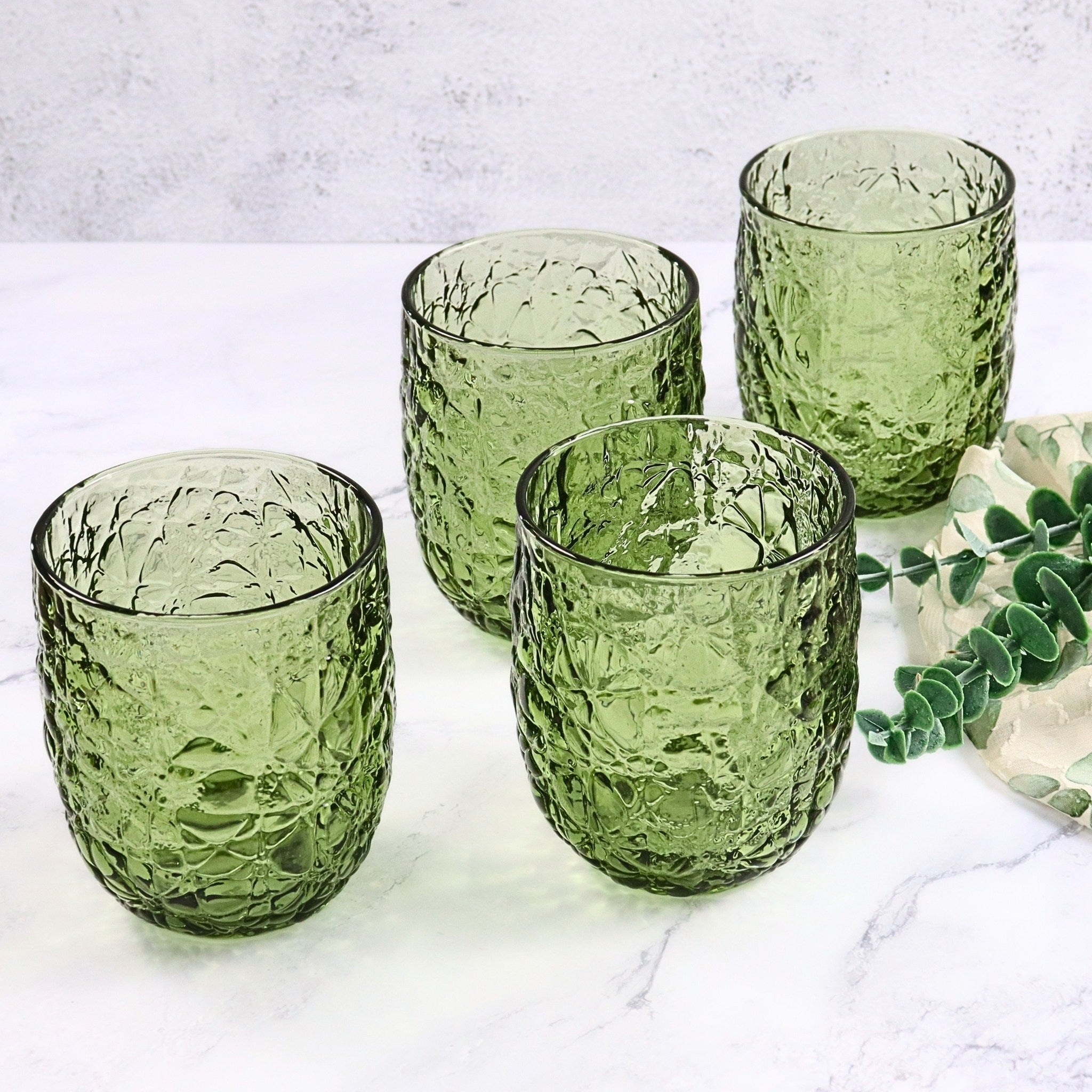 Set of four green textured glass tumblers on a light surface with a plant in the background.