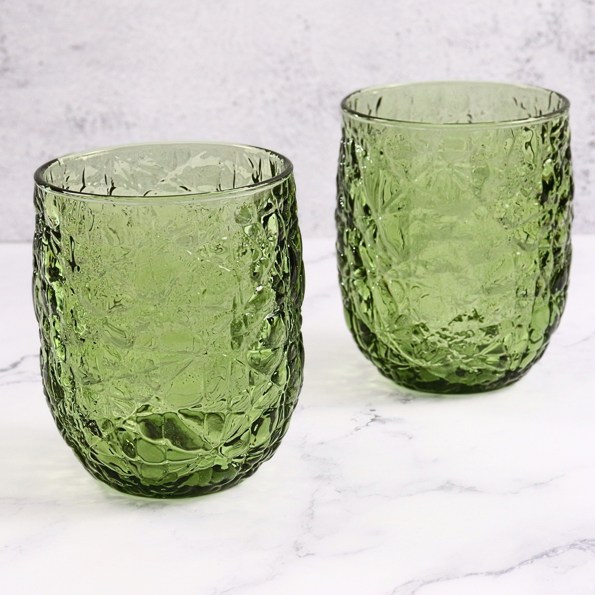 Two green textured glass tumblers on a marble surface with a light gray background