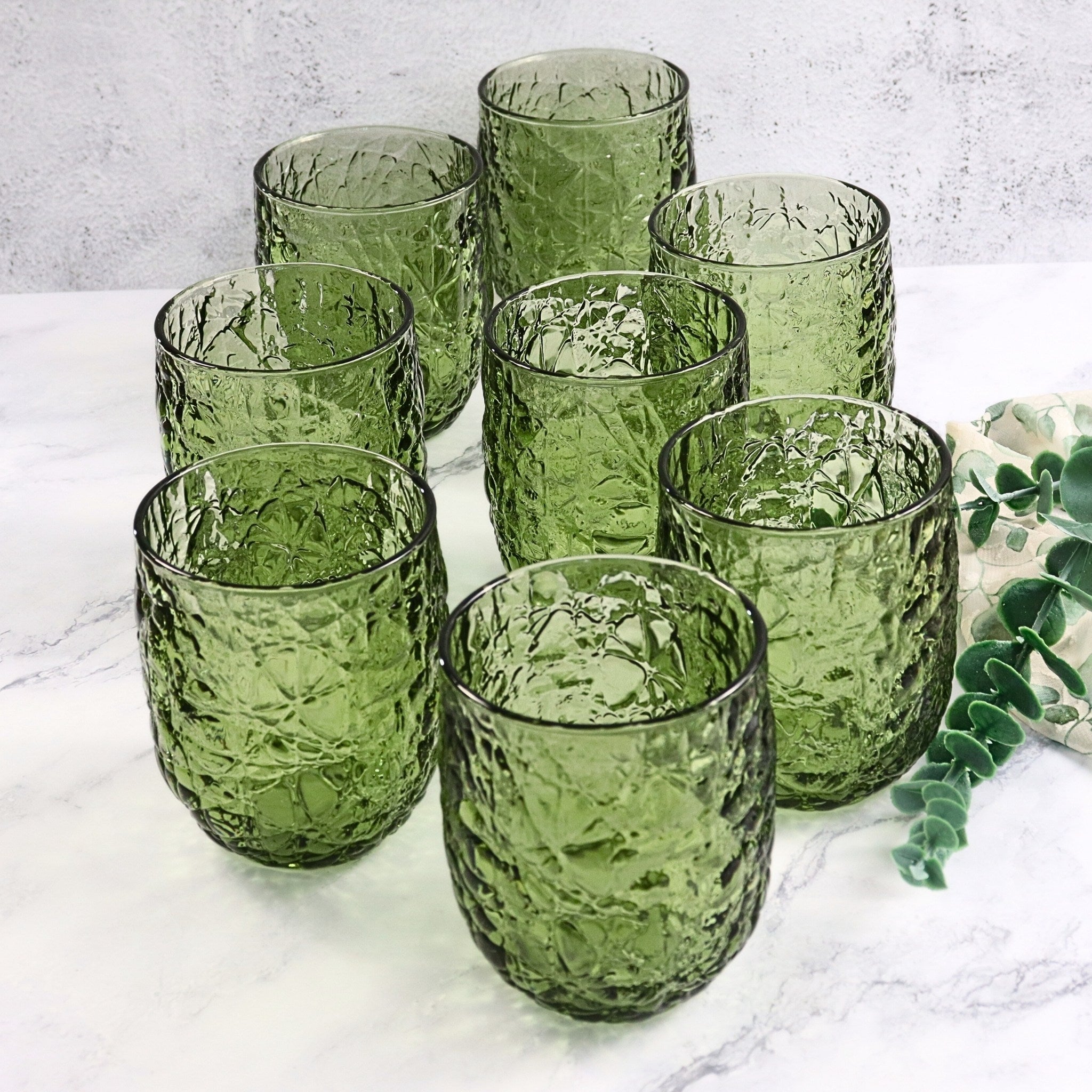 Set of green textured glass tumblers on a marble surface with a light gray background.