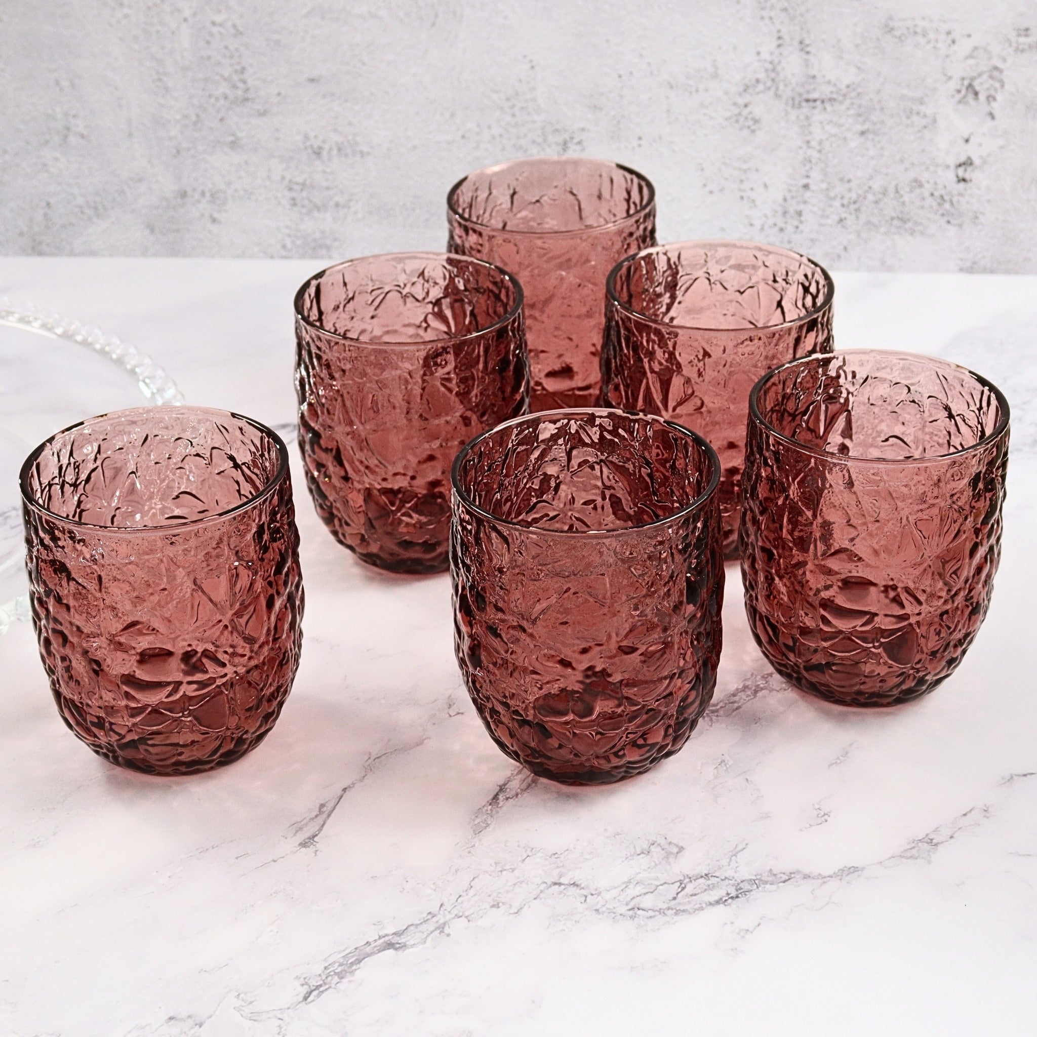 Set of six purple textured glass tumblers on a marble surface with a light gray background