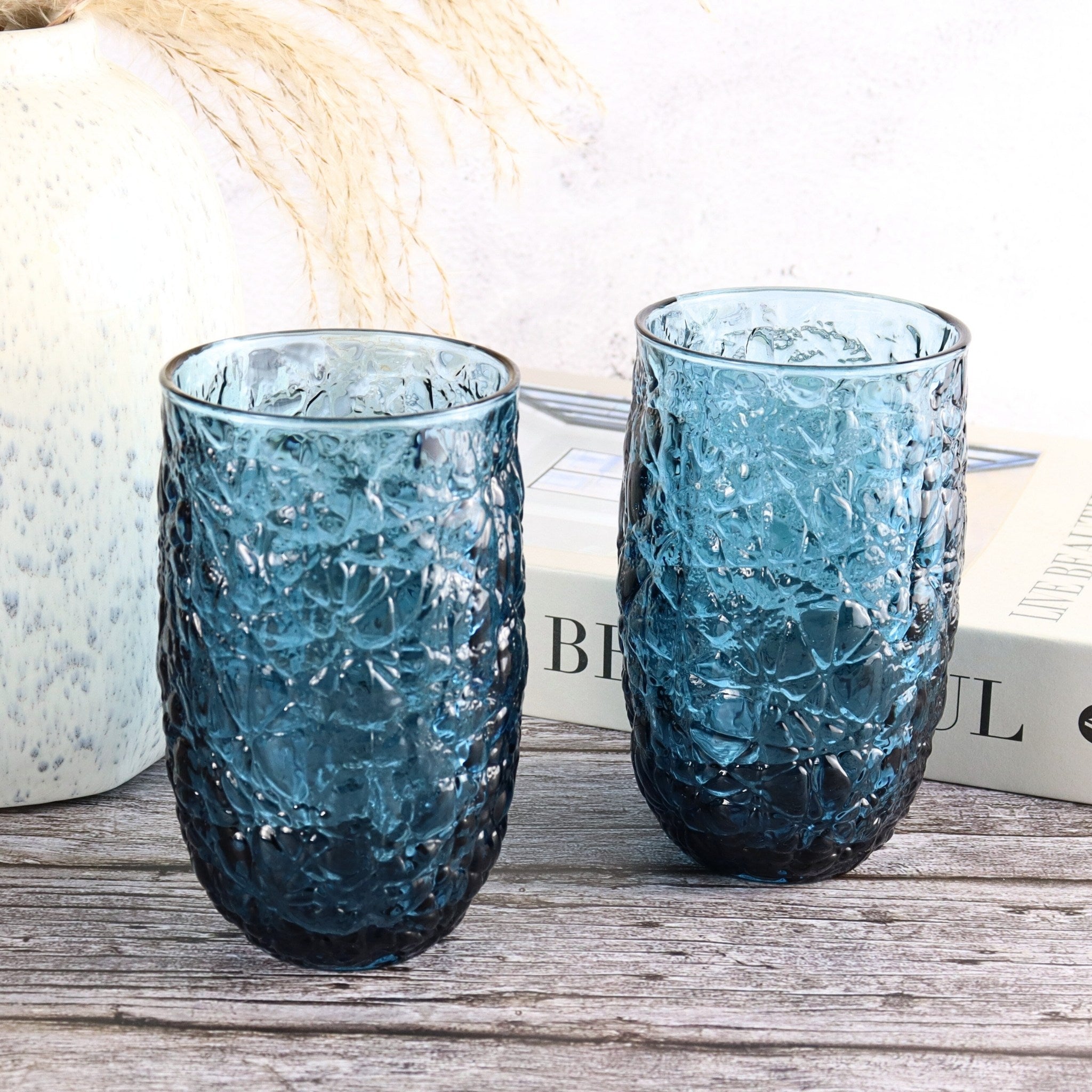 Two blue textured glass tumblers on a wooden surface with a blurred background.