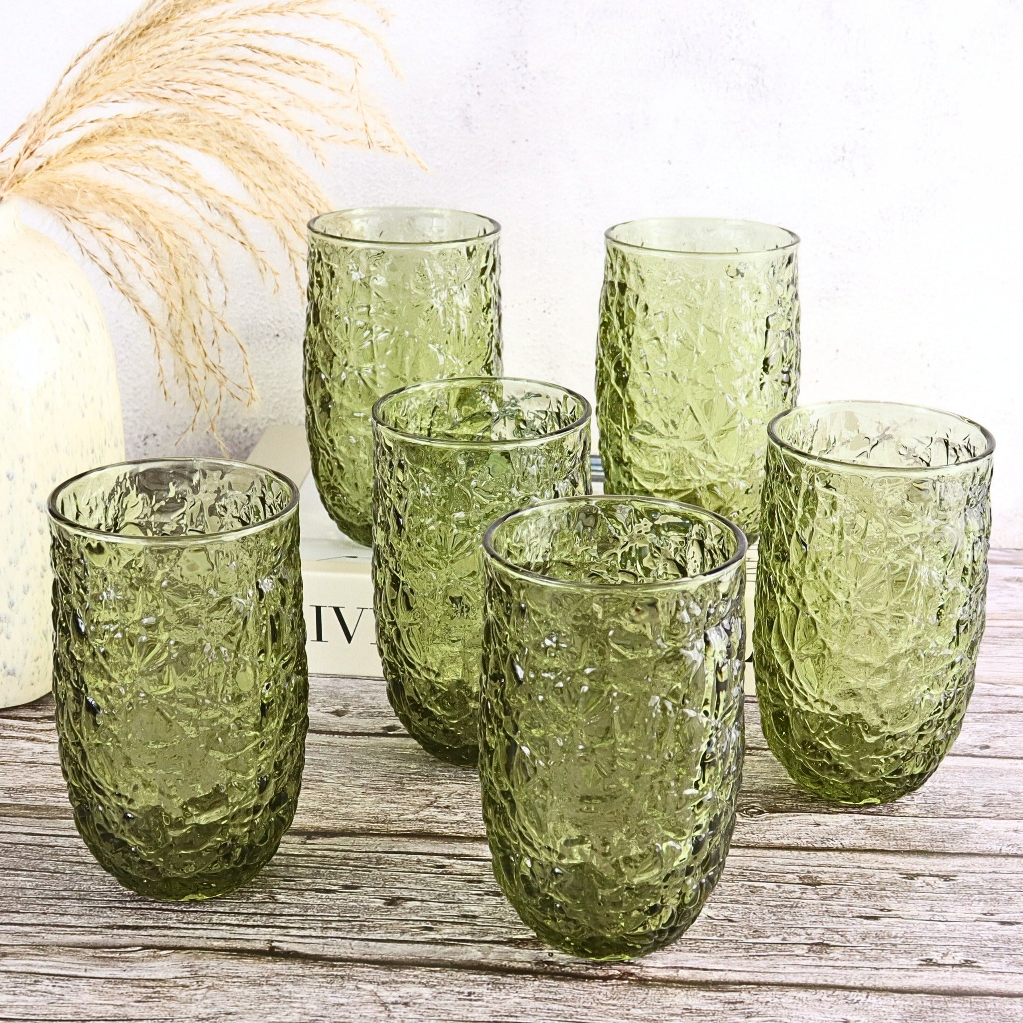 Set of green textured glass tumblers on a wooden surface with a white background