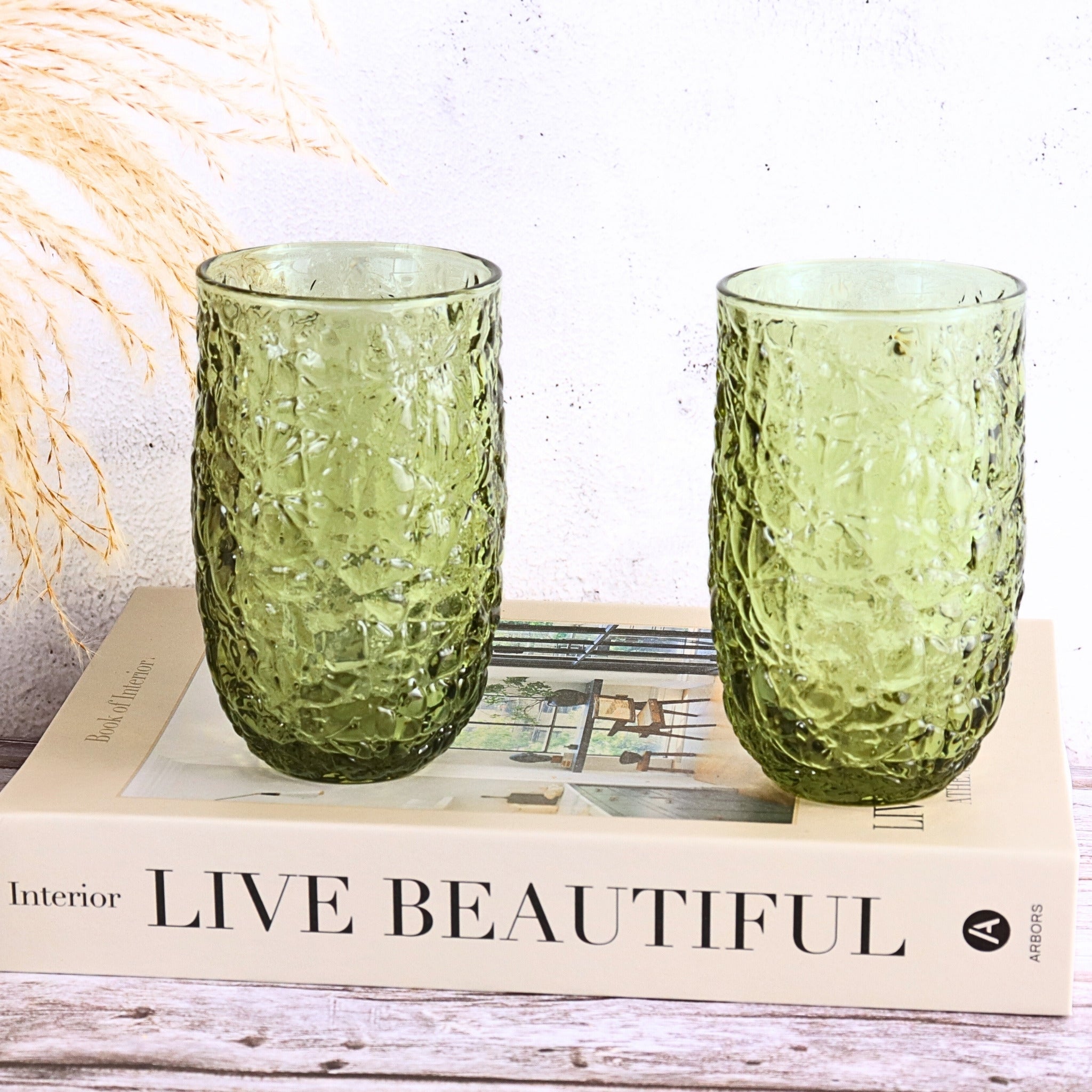 Two green textured glass tumblers on a book with 'Live Beautiful' text.