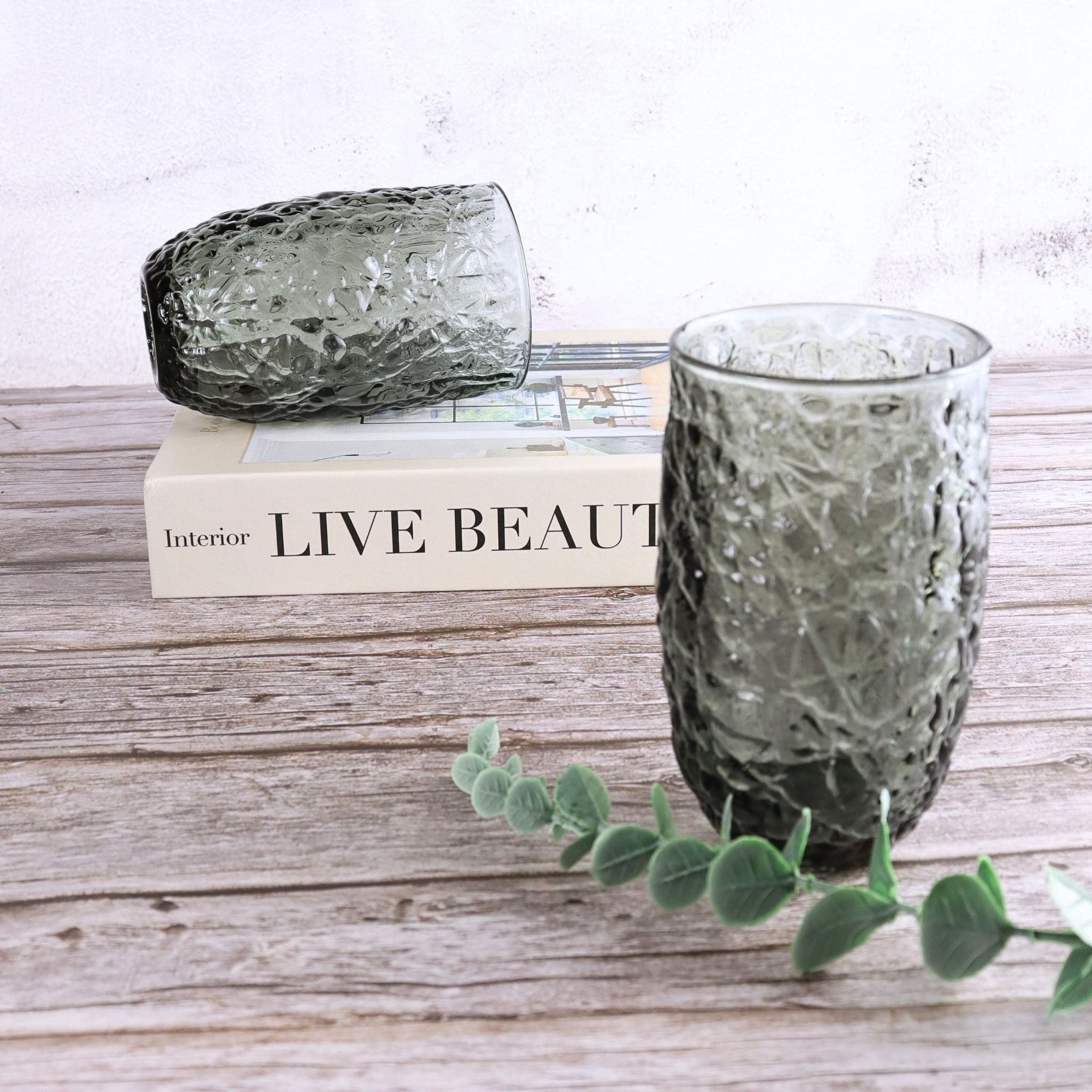 Two textured glass vases on a wooden surface with a book and eucalyptus branch.