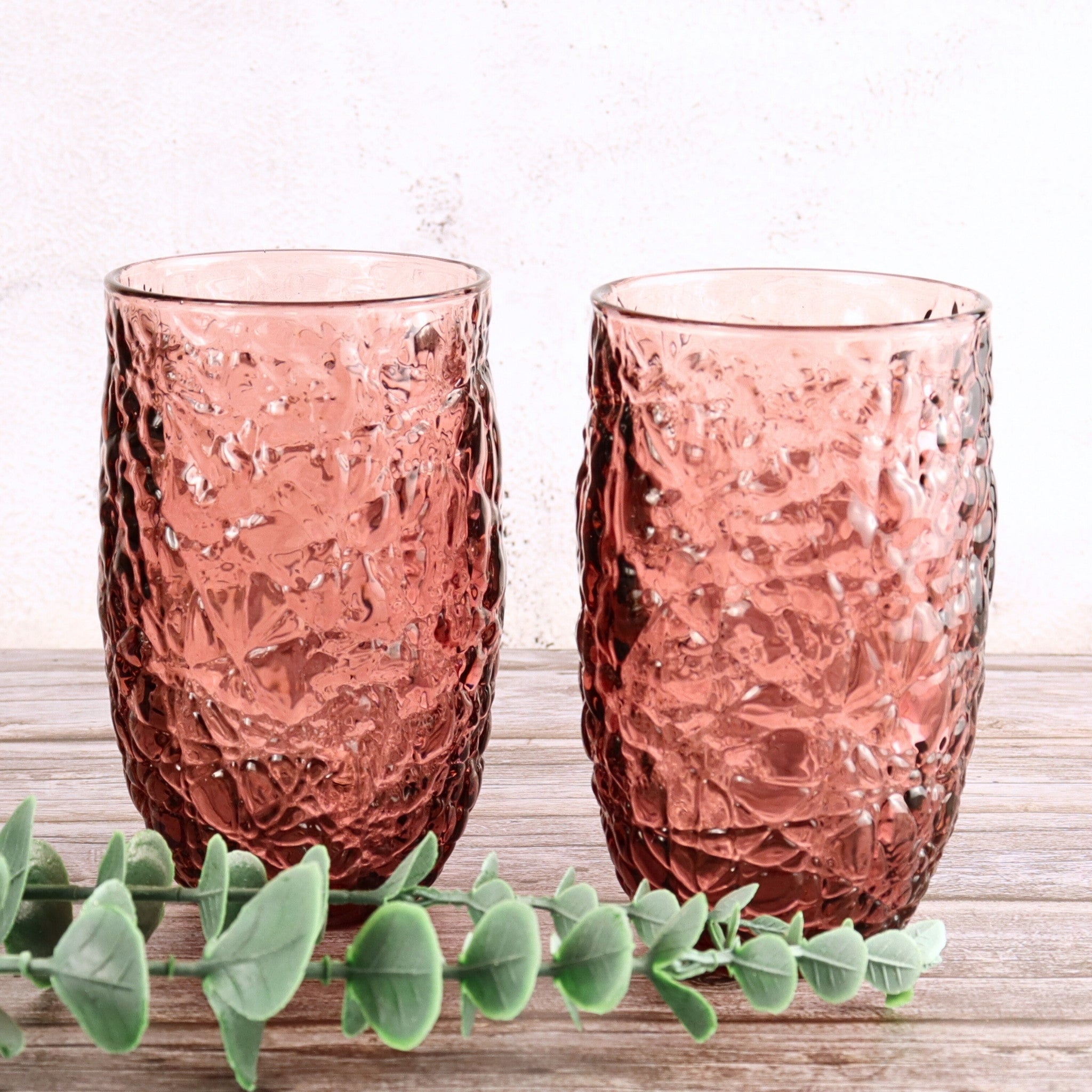 Two pink textured glass tumblers on a wooden surface with a light background
