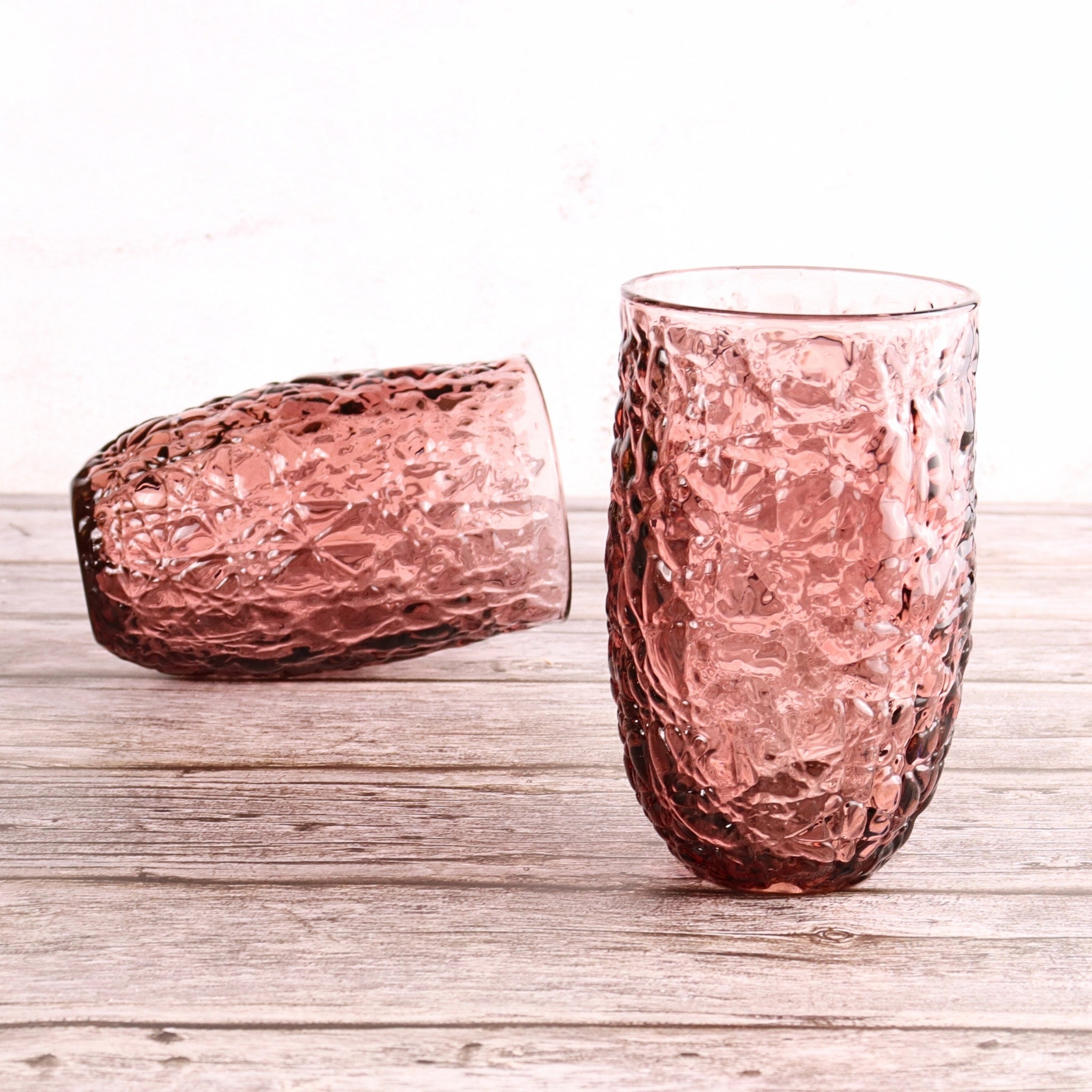 Two pink textured glass tumblers on a wooden surface