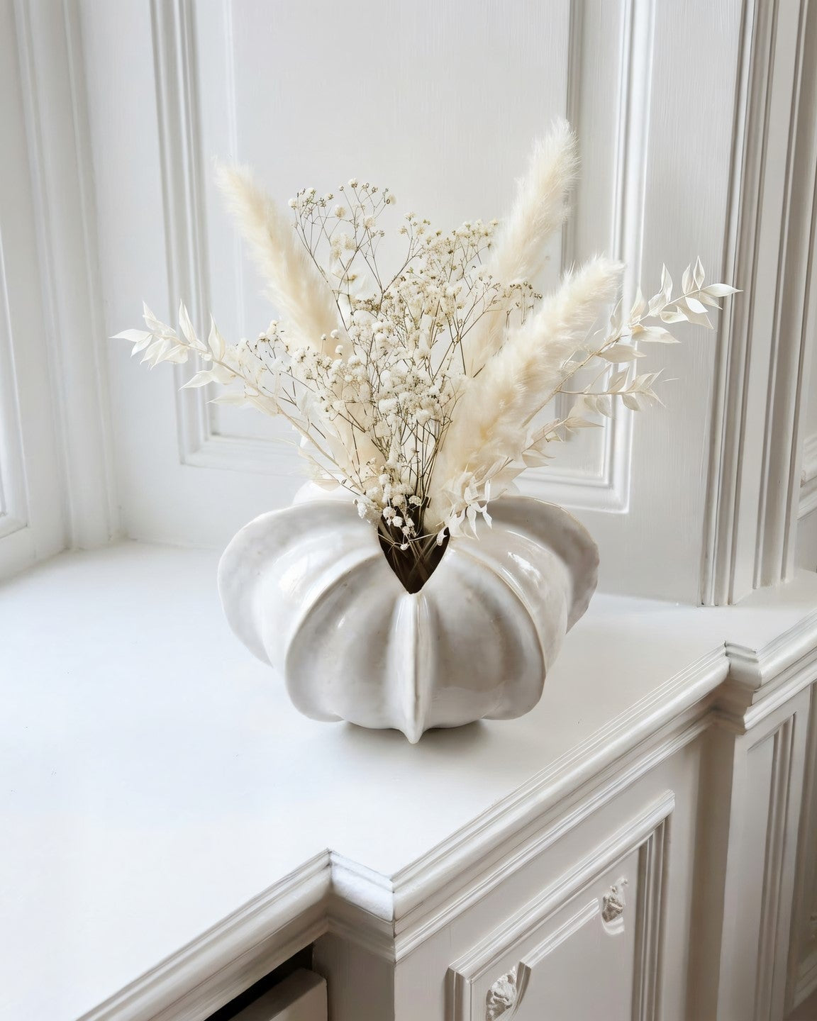 White ceramic vase with dried flowers on a white surface