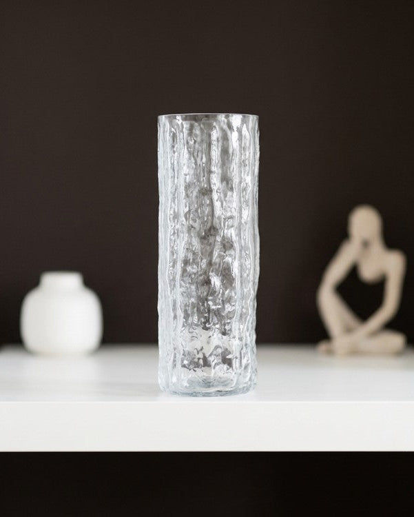 Clear textured vase with white flowers on a wooden surface with a book in the background
