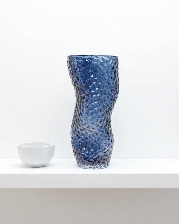 Blue textured vase with white flowers on a light gray surface with a book underneath.