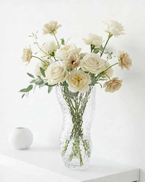 Clear textured vase with white flowers on a wooden surface next to books