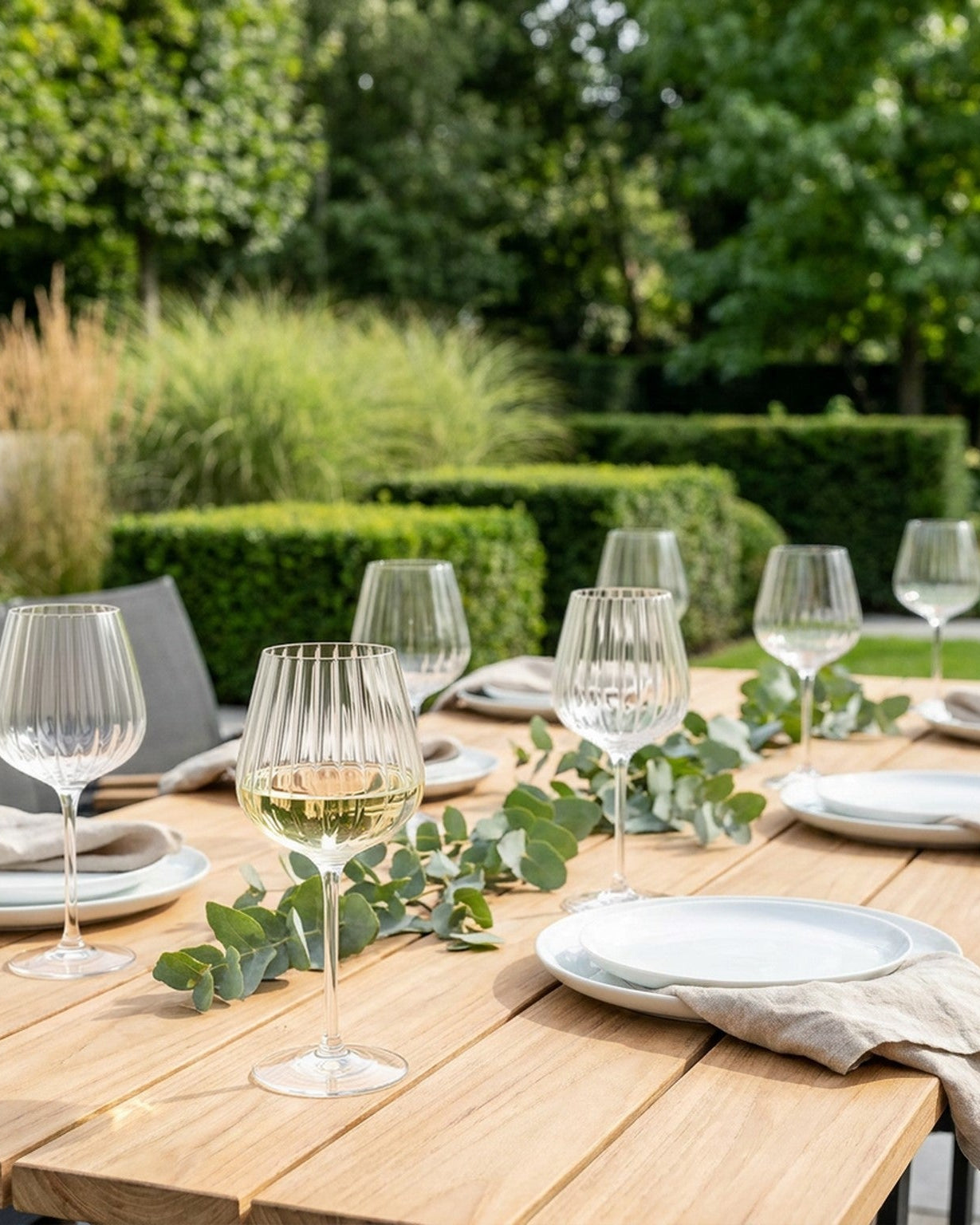 clear ribbed wine goblet glasses, on a garden table with greenery in background.