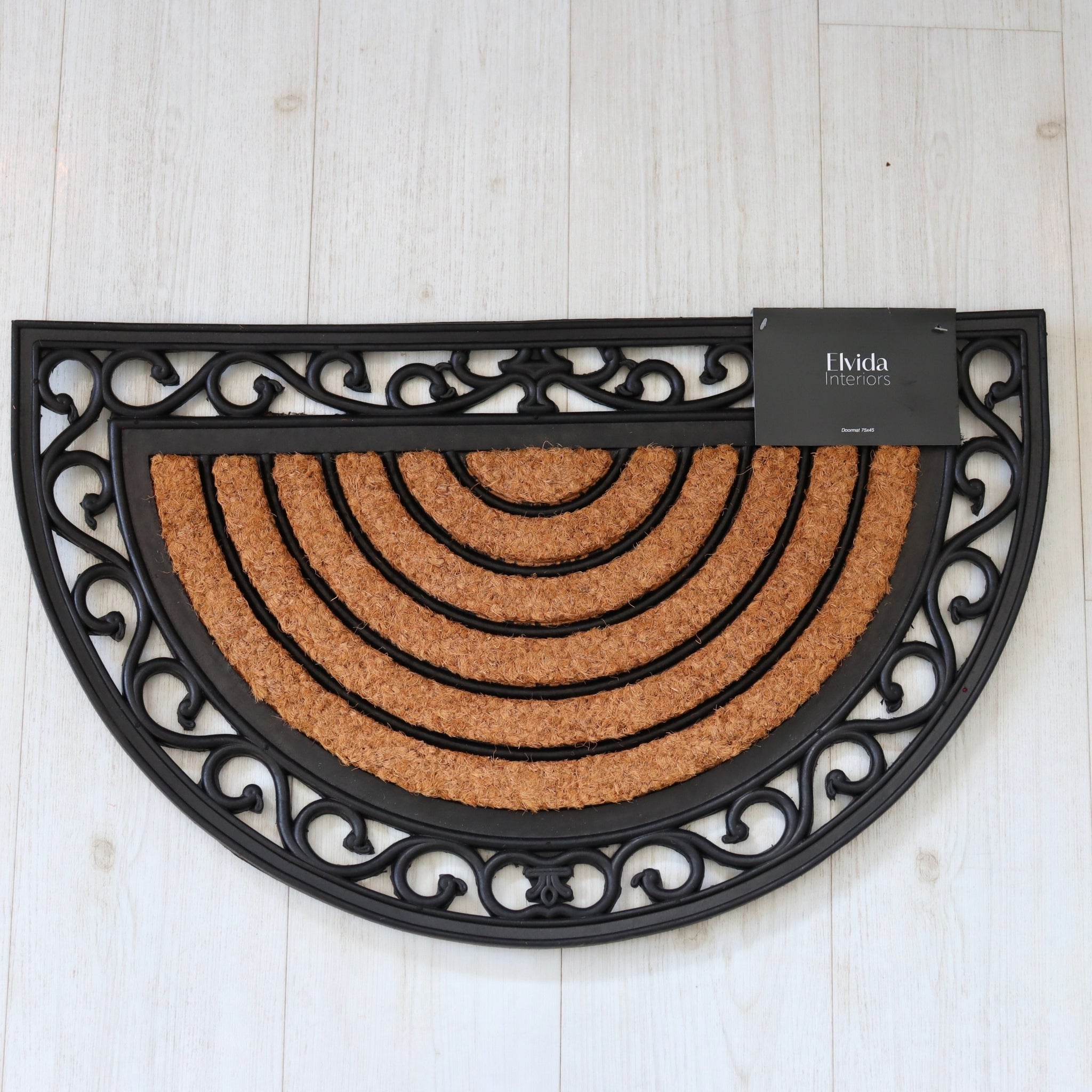 Half-circle doormat with decorative black border on a light wooden floor, featuring the brand 'Elvida Interiors'.