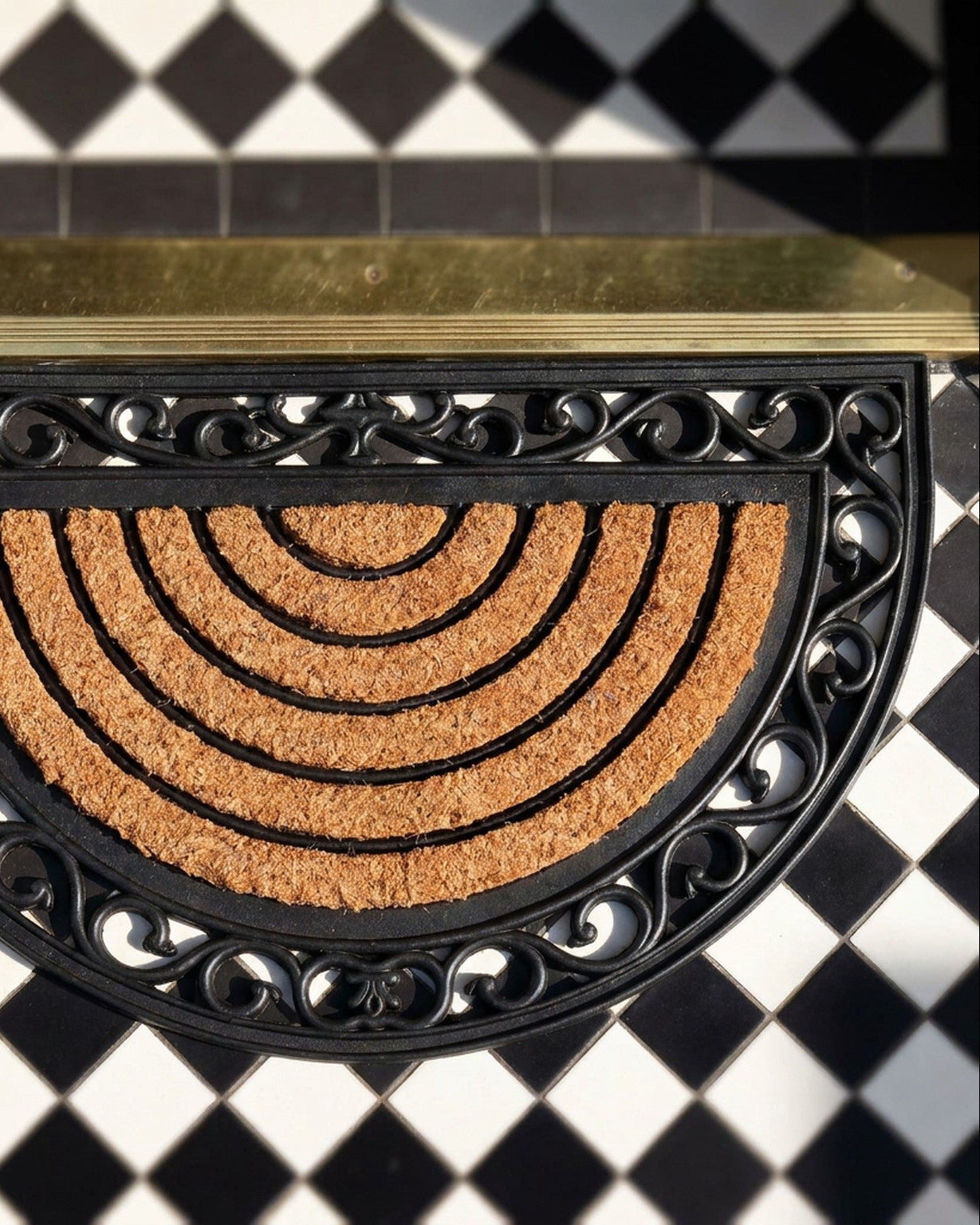 Decorative doormat with black metal border on a black and white checkered floor.