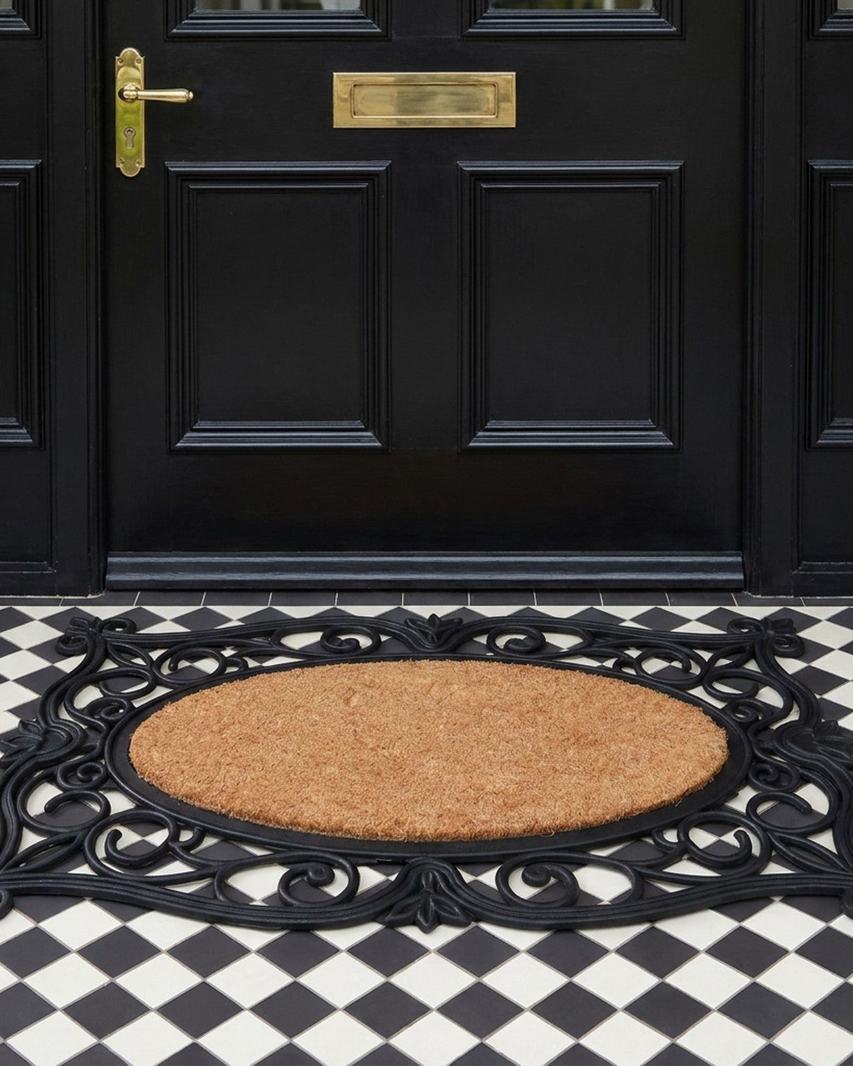 Decorative doormat with intricate design in front of a black door on a checkered floor.