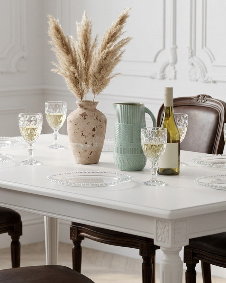 Dining table set with wine glasses, bottles, and decorative elements in a bright room.