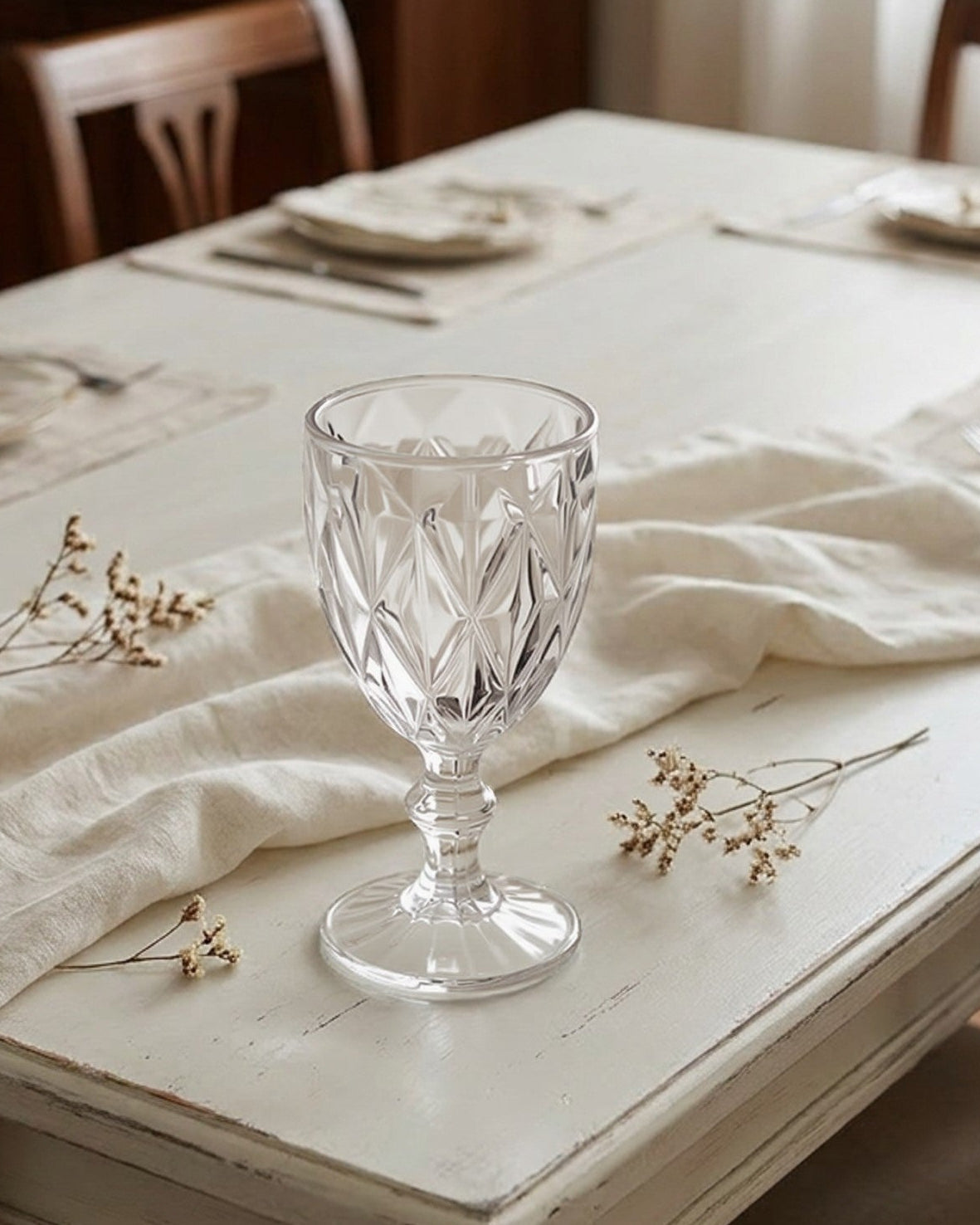 Dining table set with plates, glasses, and a crystal glass in a softly lit room.