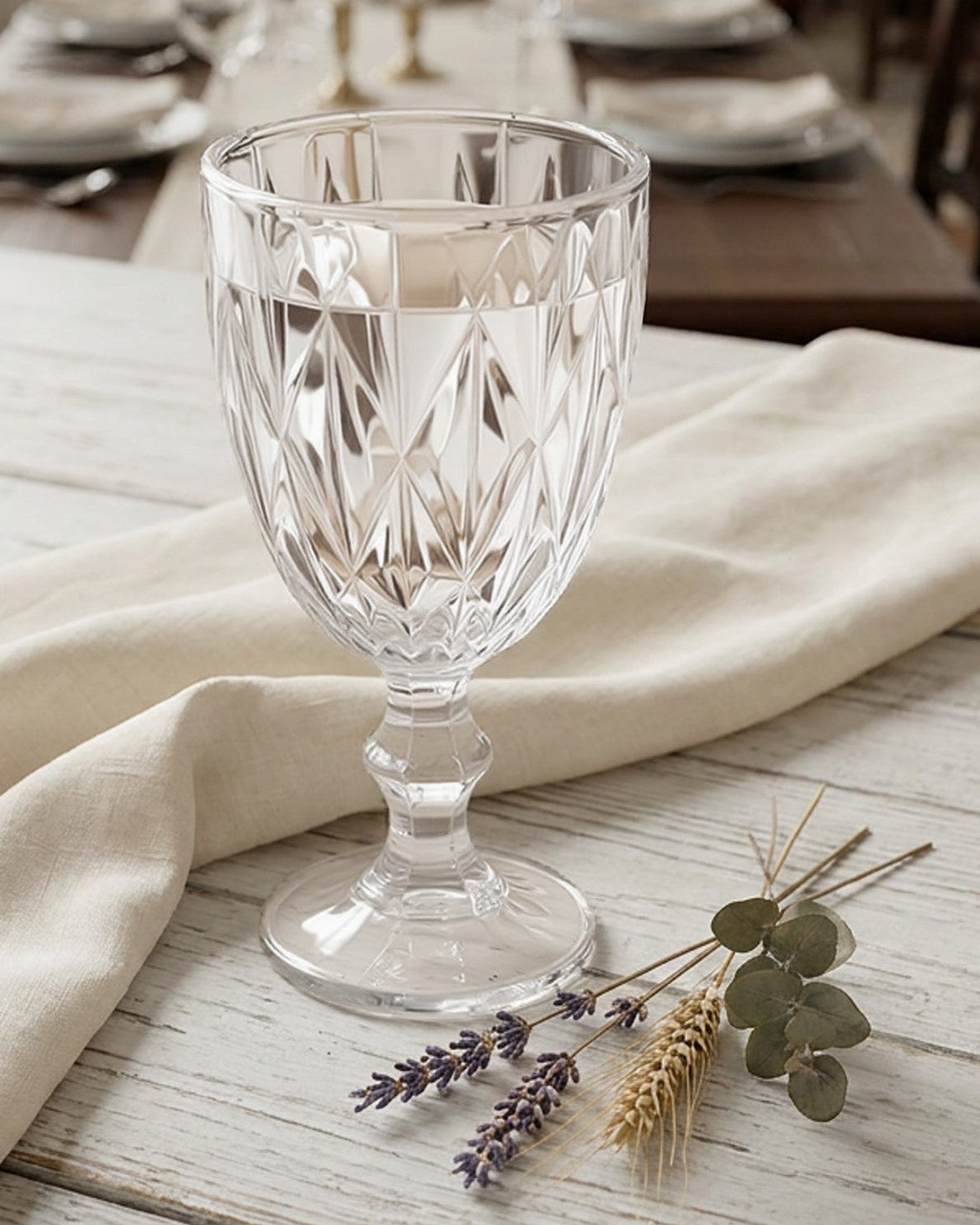 Clear glass goblet on a wooden table with a beige cloth and decorative elements.