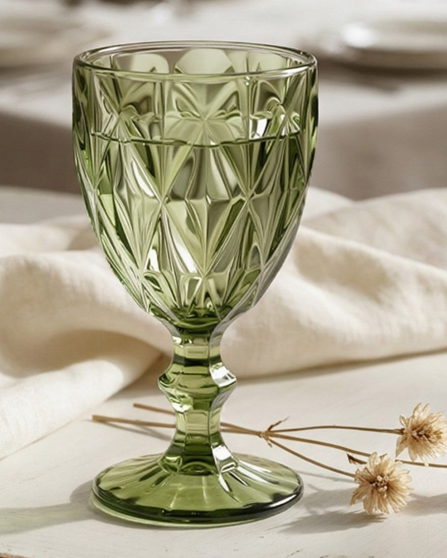 Set of green glass goblets on a wooden surface with a blurred book in the background.