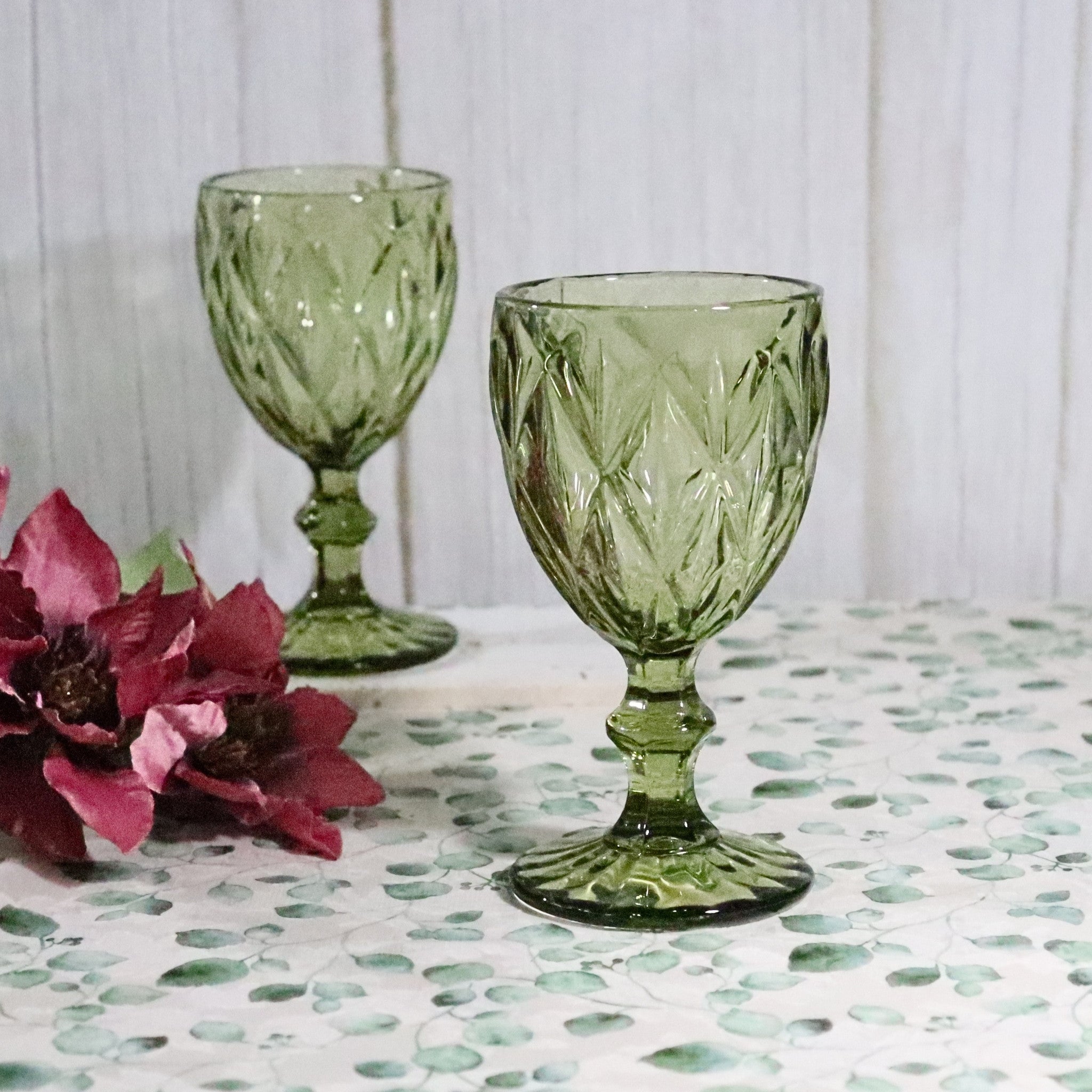 Two green glass goblets on a patterned surface with pink flowers.