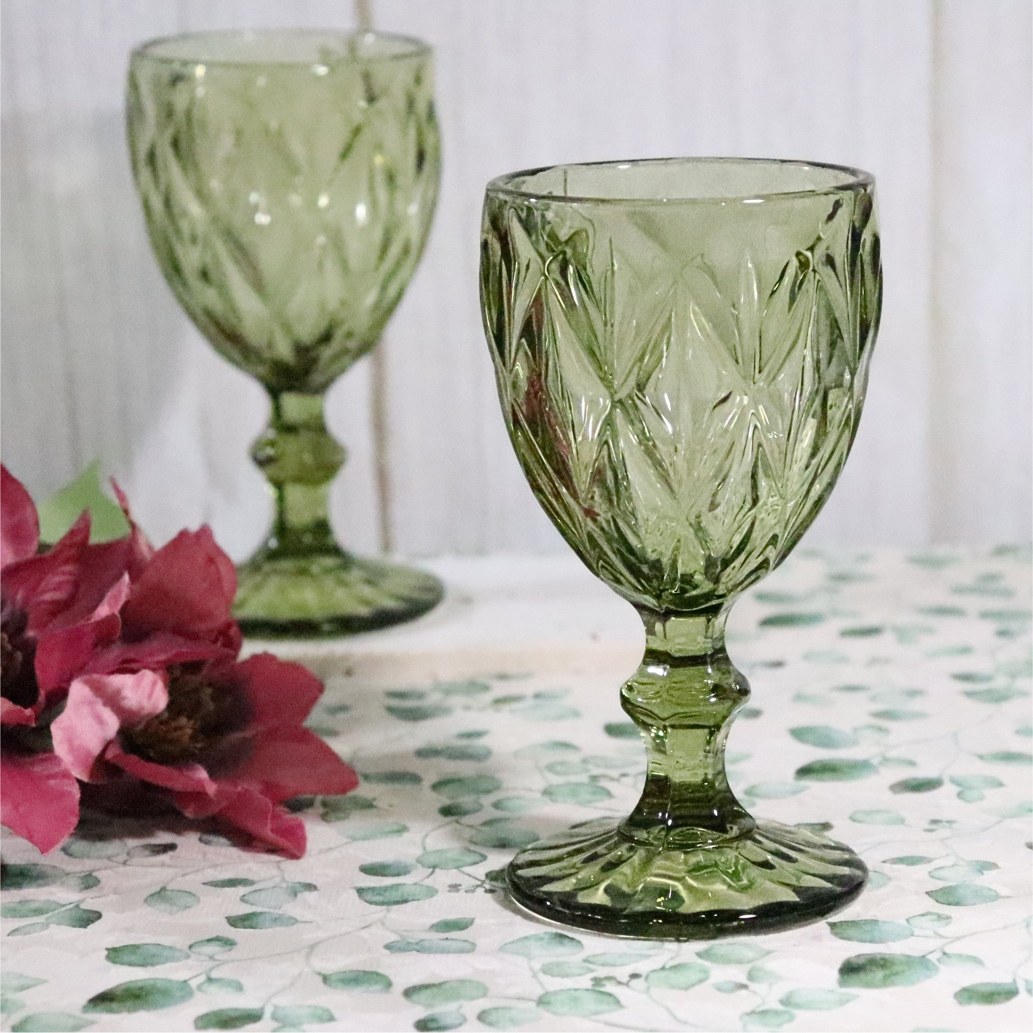 Two green glass goblets with floral arrangement on a patterned surface