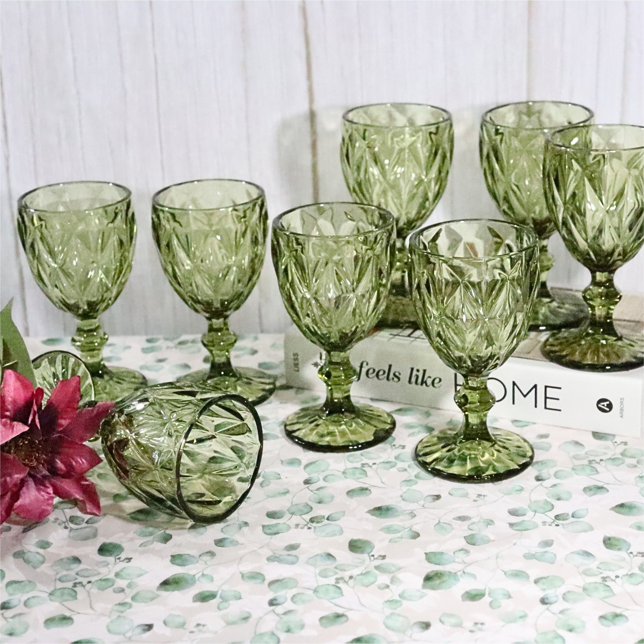 Set of green glass goblets on a patterned surface with a white wooden background