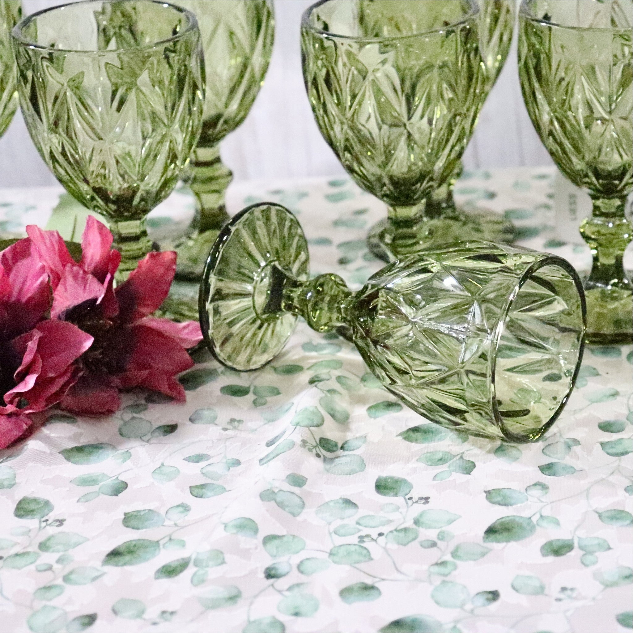 Set of green glass goblets on a patterned tablecloth with pink flowers.