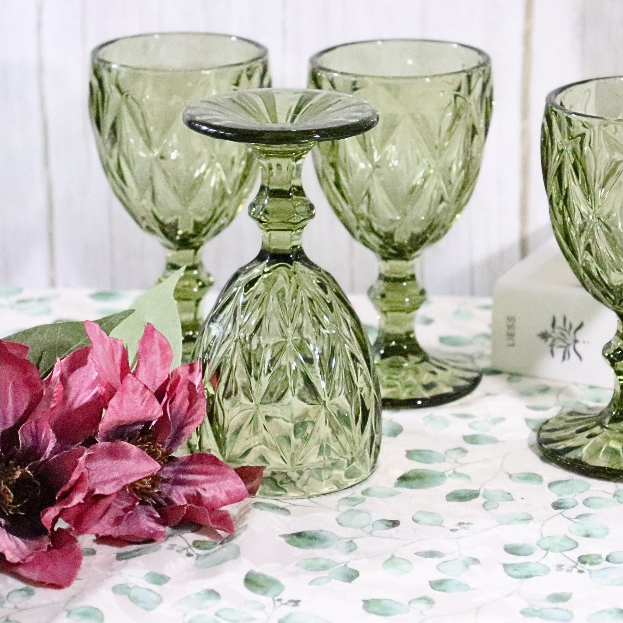 Set of green glass goblets on a table with flowers and a candle.