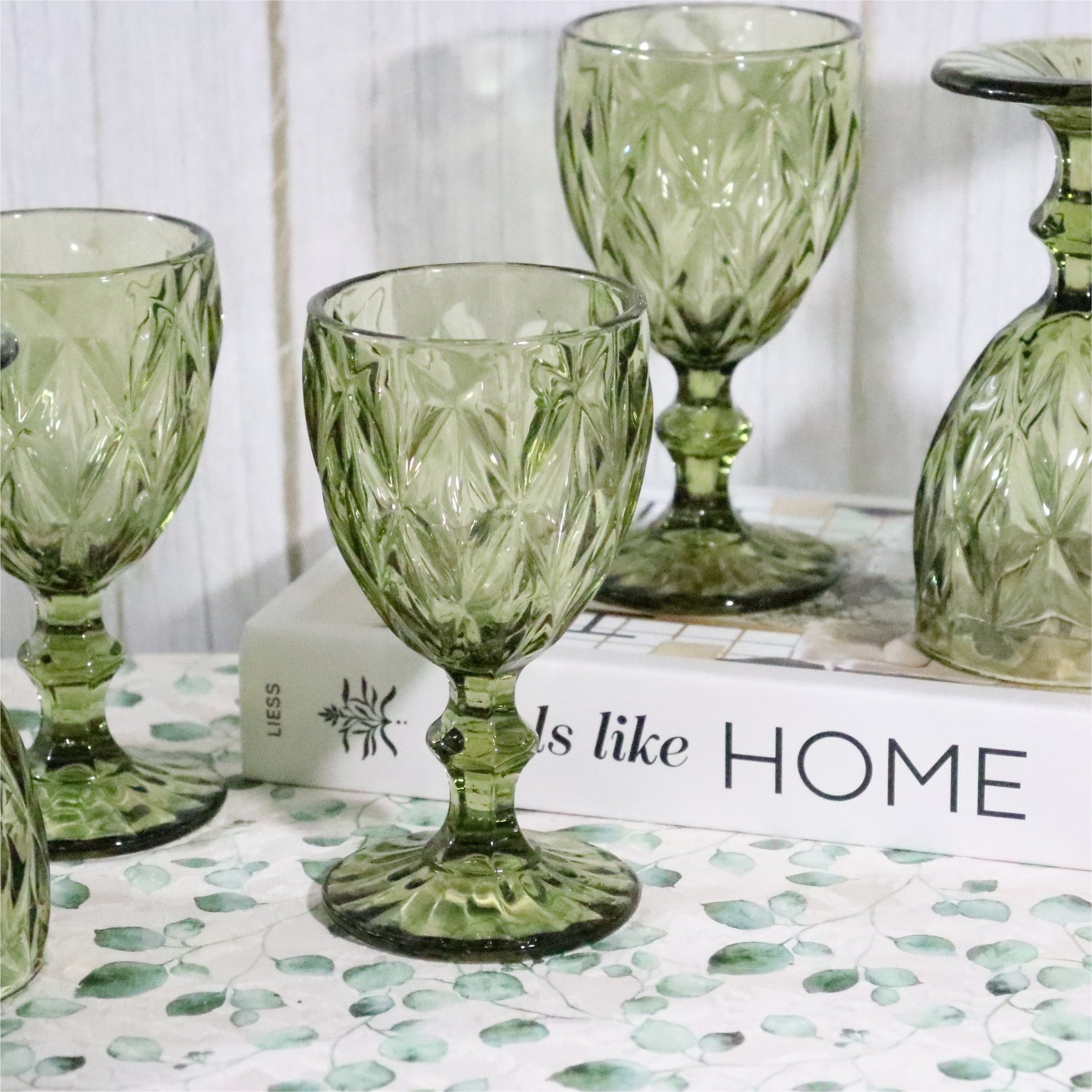 Set of green glass goblets on a surface with a 'Home' themed book in the background.