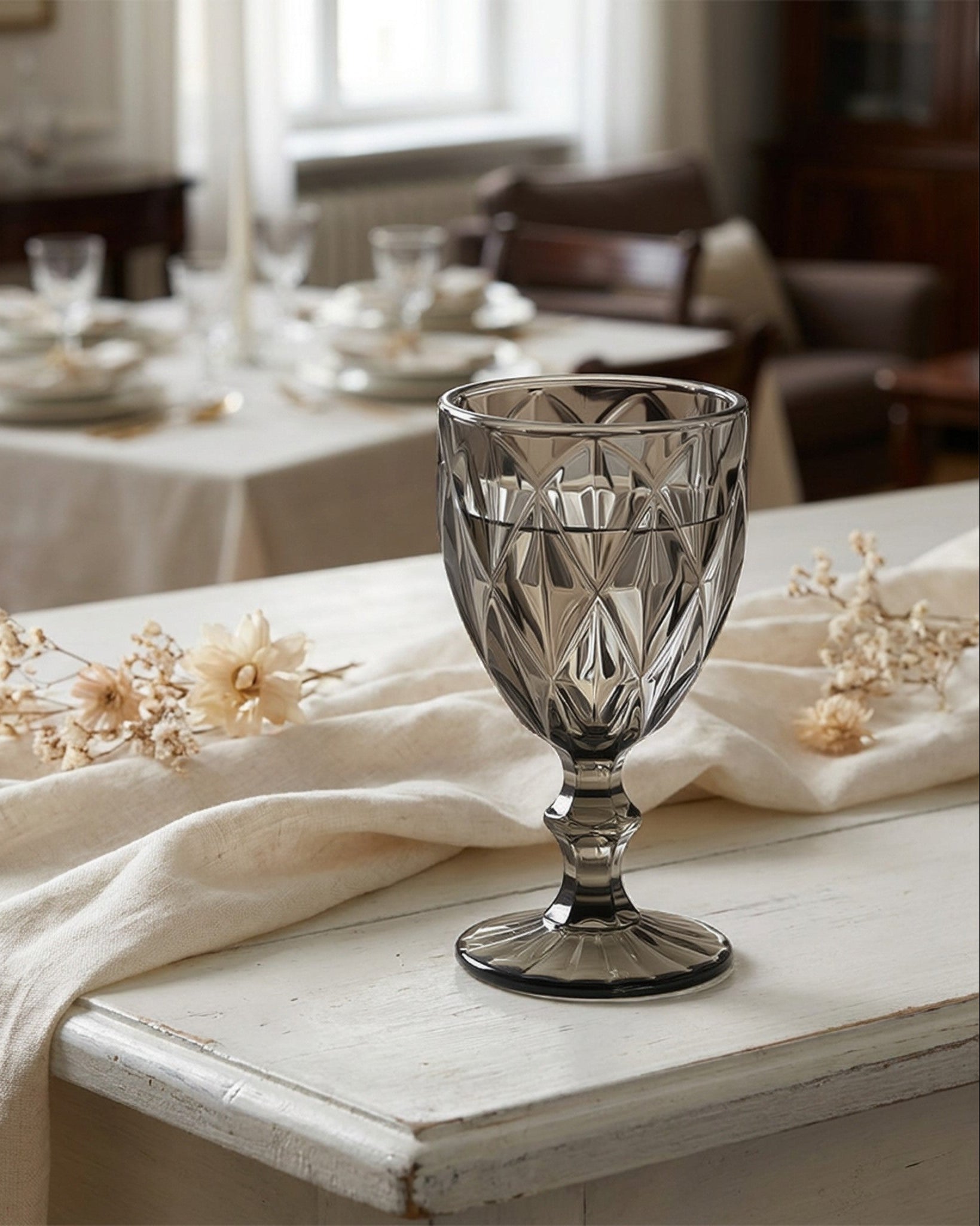Decorative crystal goblet on a table with a white cloth and floral arrangements.