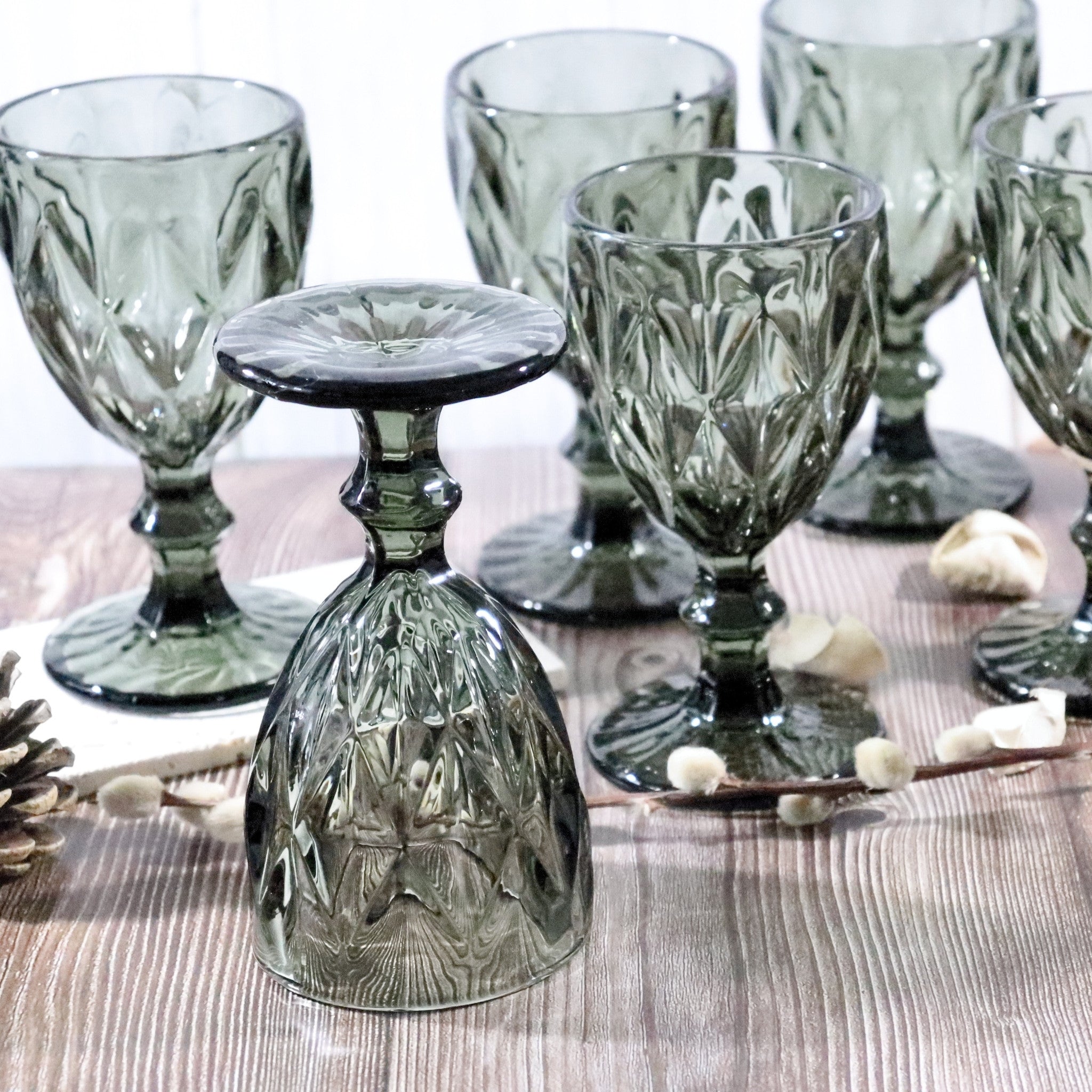 Set of grey glass goblets on a wooden surface with decorative elements.