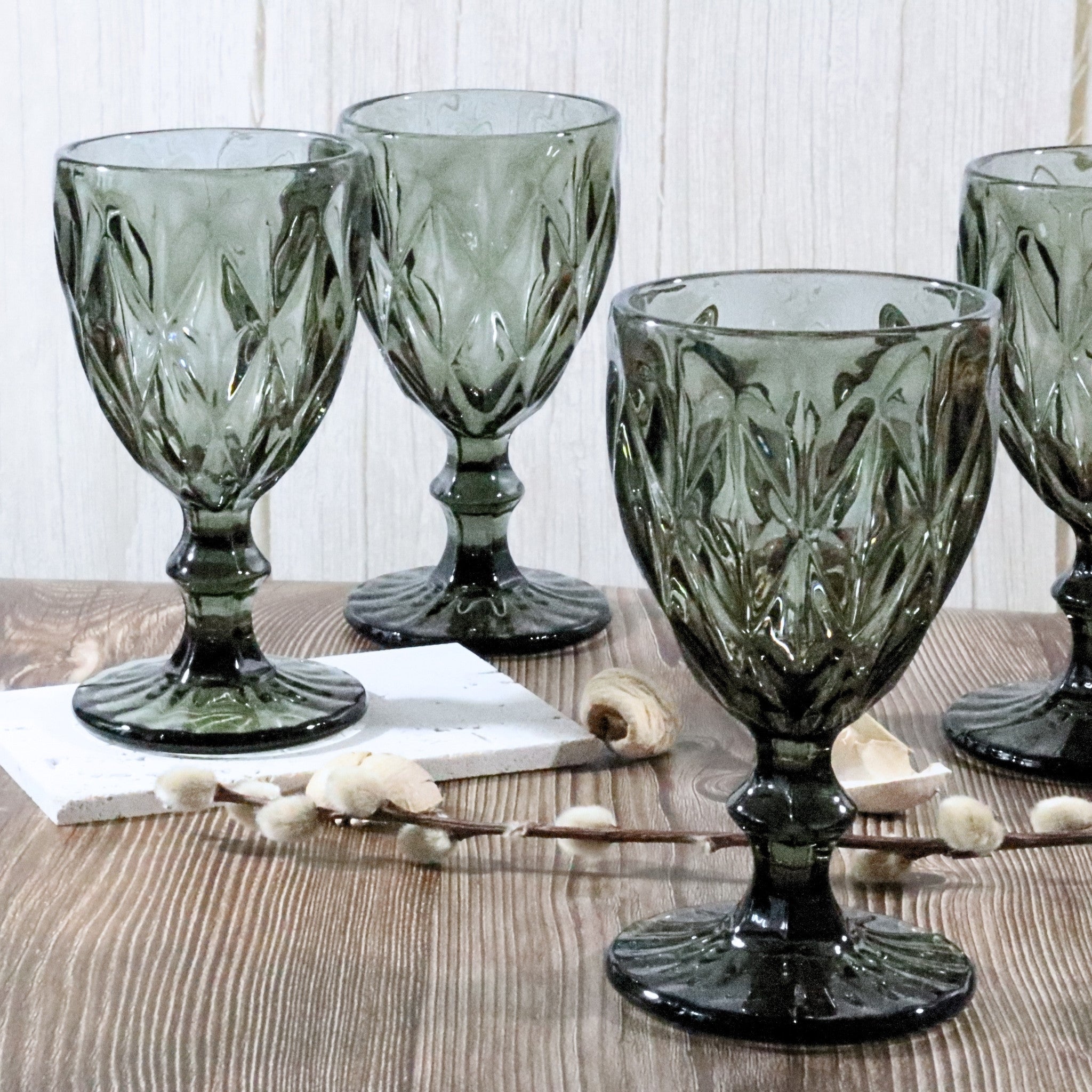 Set of four grey glass goblets on a wooden surface with a white background