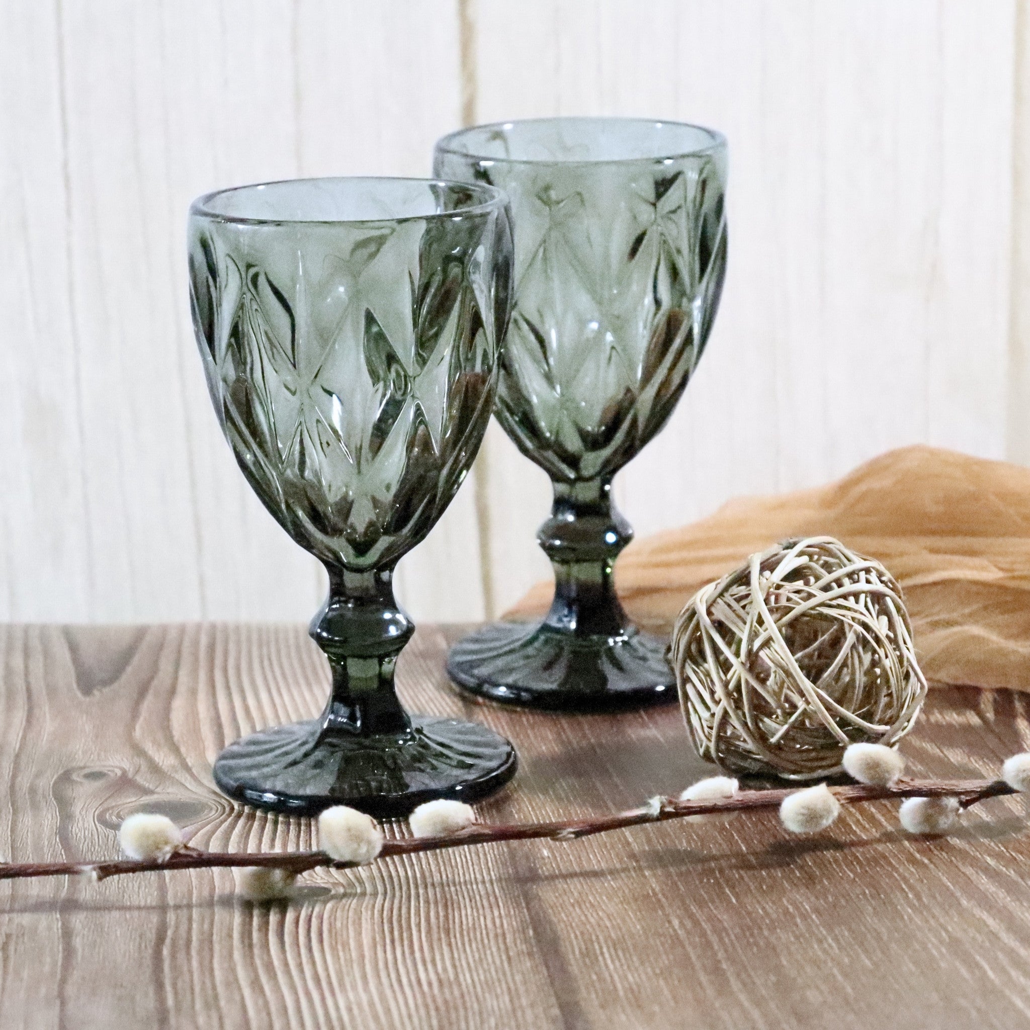 Two grey glass goblets on a wooden surface with decorative elements.