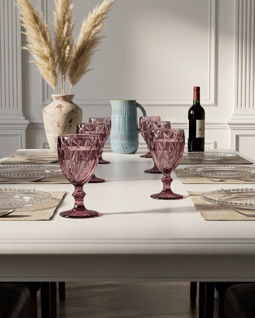 Dining table set with pink glasses, a vase, and a bottle of wine in a room with white walls and wooden paneling.