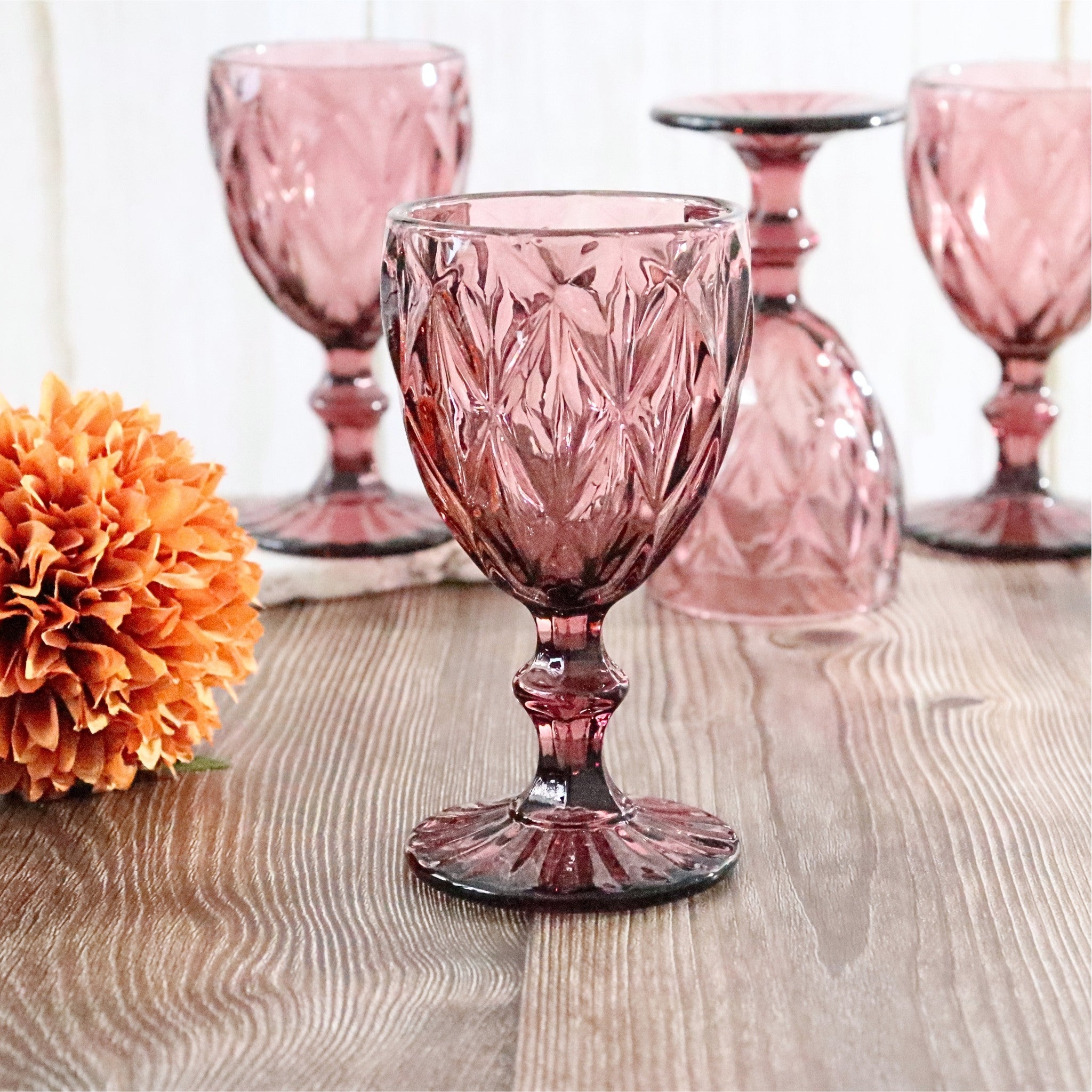 Set of purple glass goblets on a wooden surface with an orange flower.