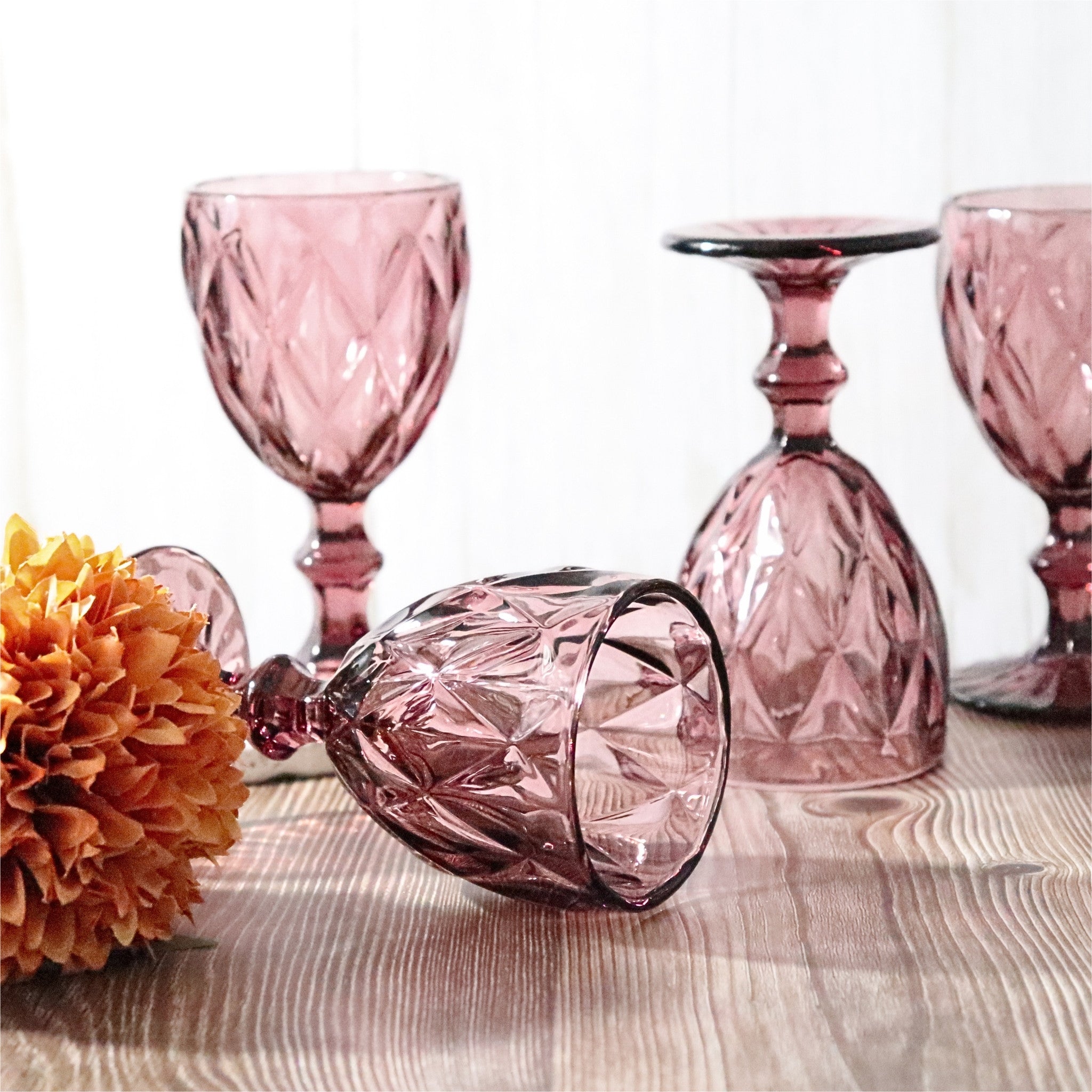 Set of purple glassware including goblets and a candle holder on a wooden surface with flowers.