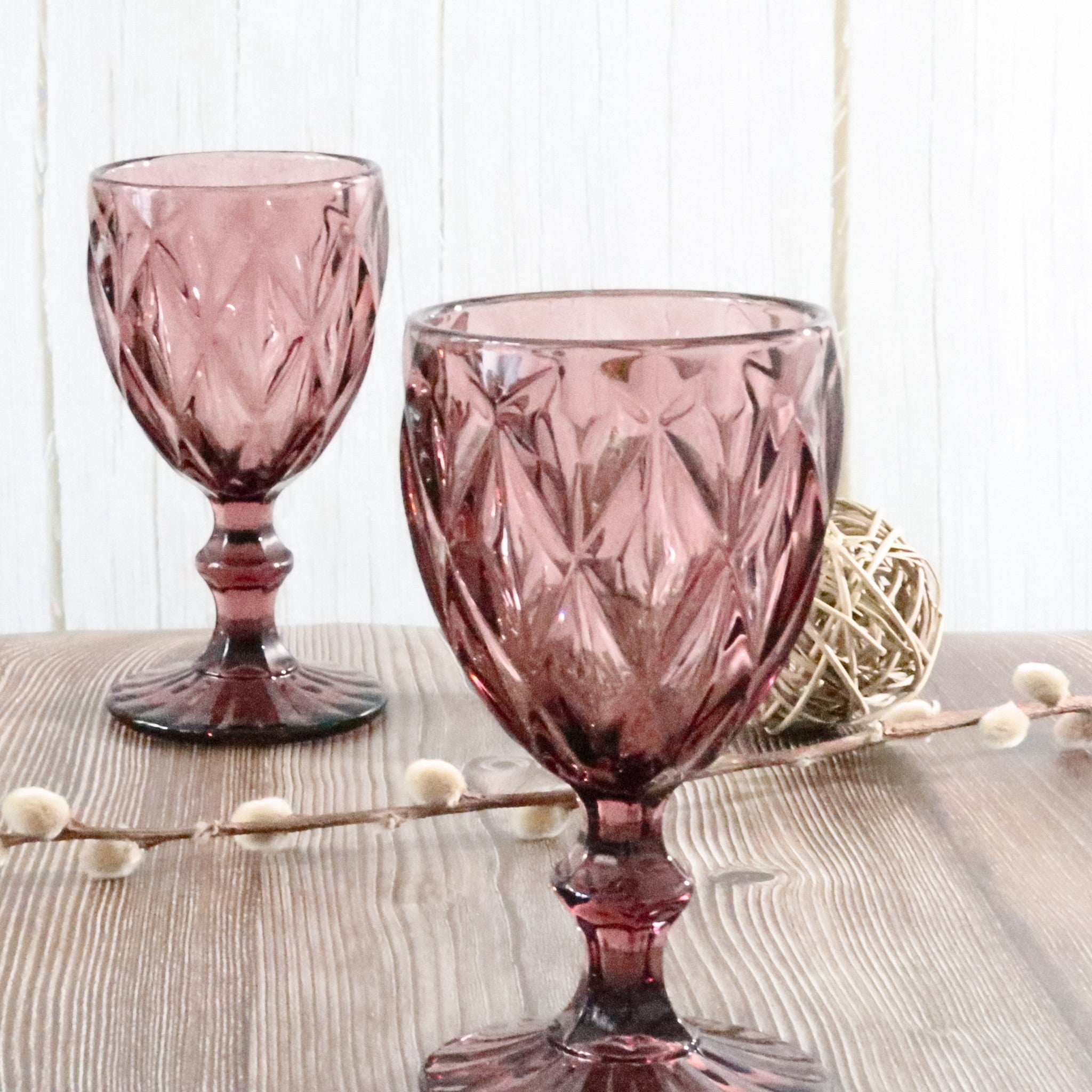 Two purple glass goblets on a wooden surface with a white background