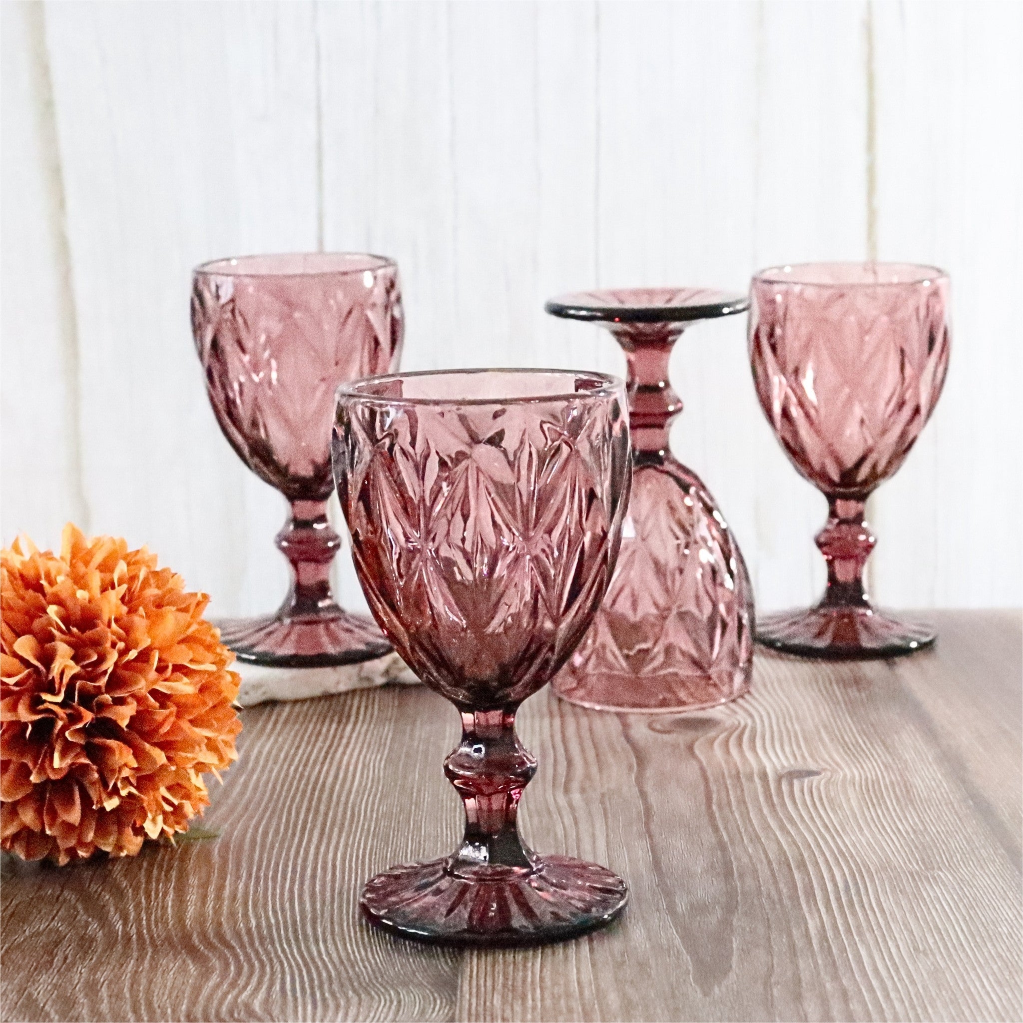 Set of purple glass goblets on a wooden surface with an orange flower.